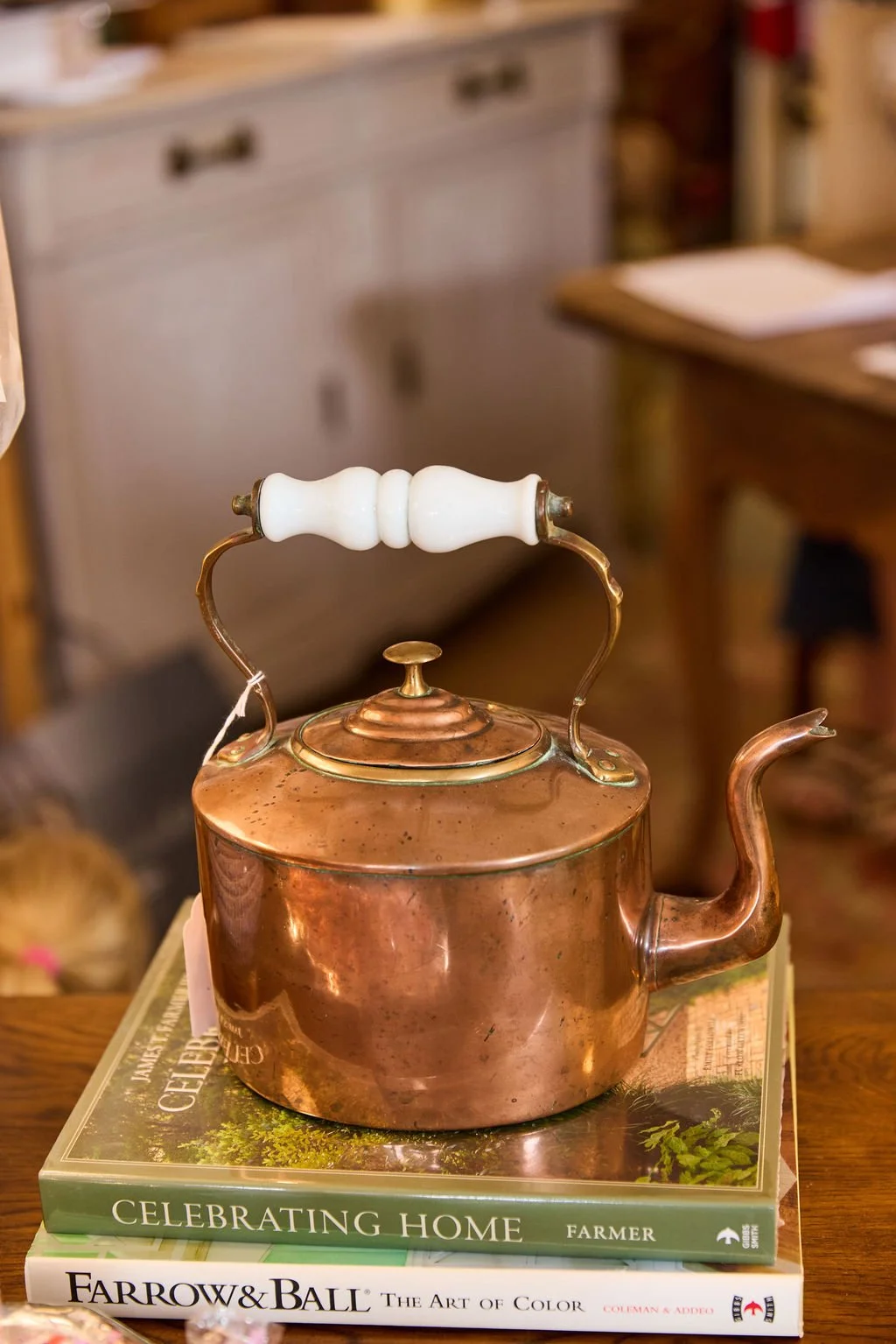 Vintage copper tea kettle with a white ceramic handle displayed on stacked design books.