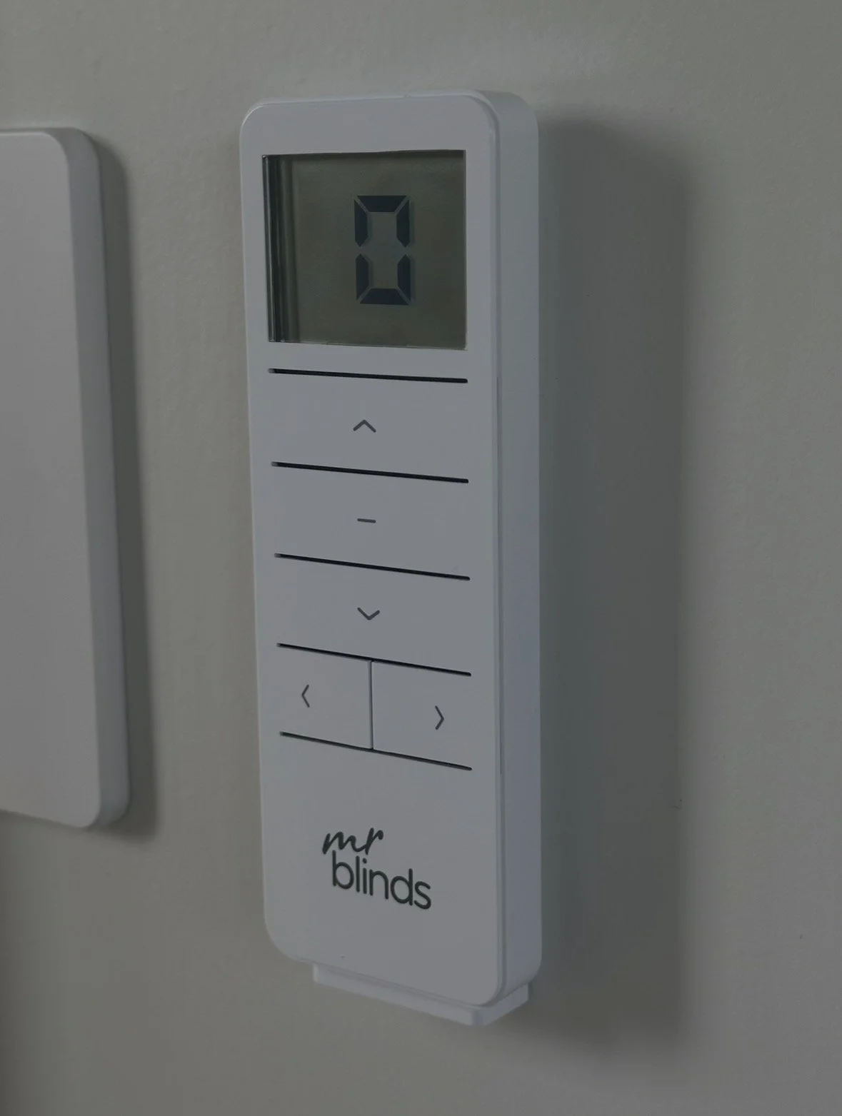 White Mr. Blinds remote control mounted on a wall, displaying 20 on its digital screen