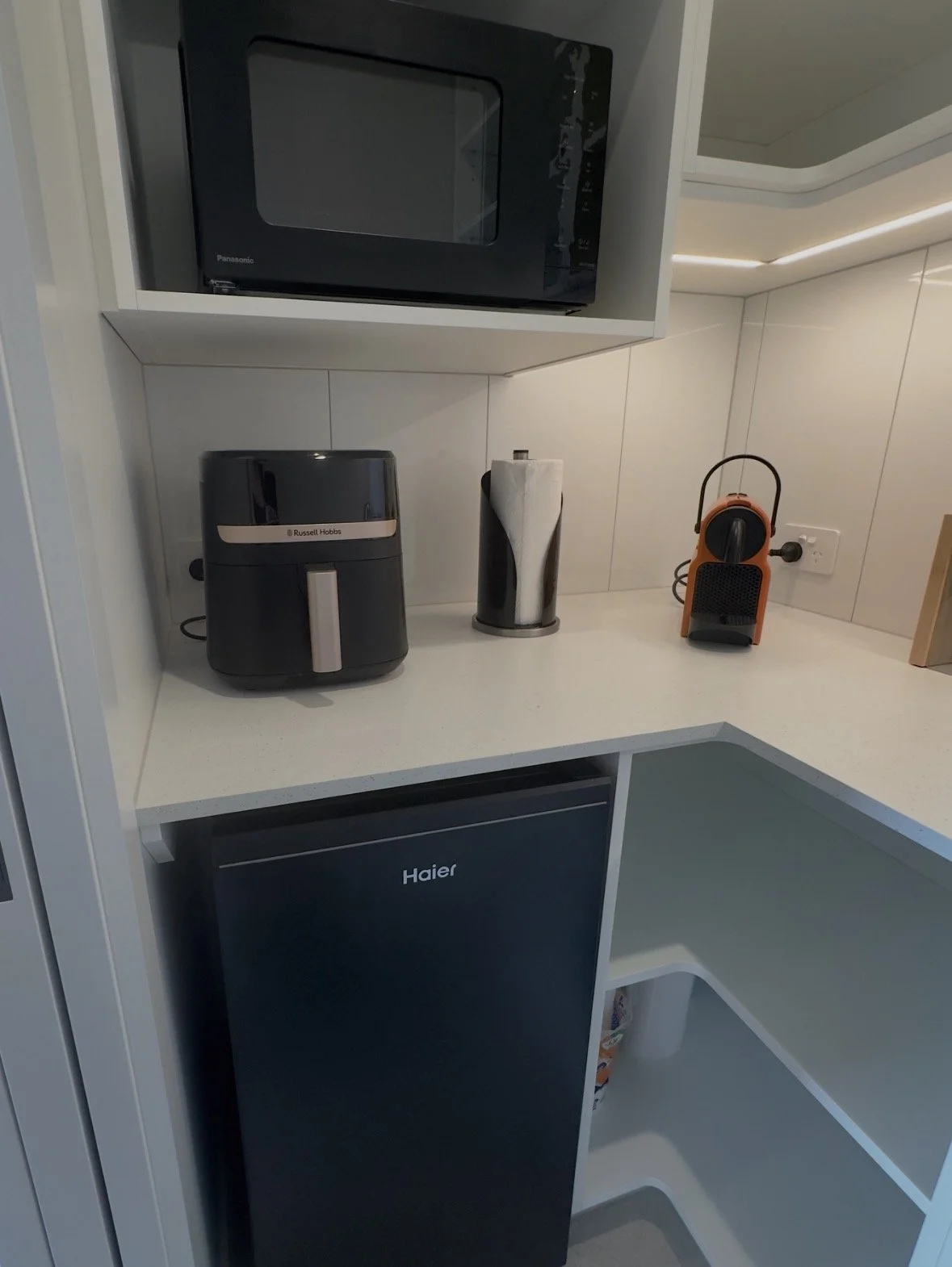 Compact white kitchen with a Panasonic microwave, Russell Hobbs air fryer, Nespresso coffee machine, paper towel holder, and Haier refrigerator.