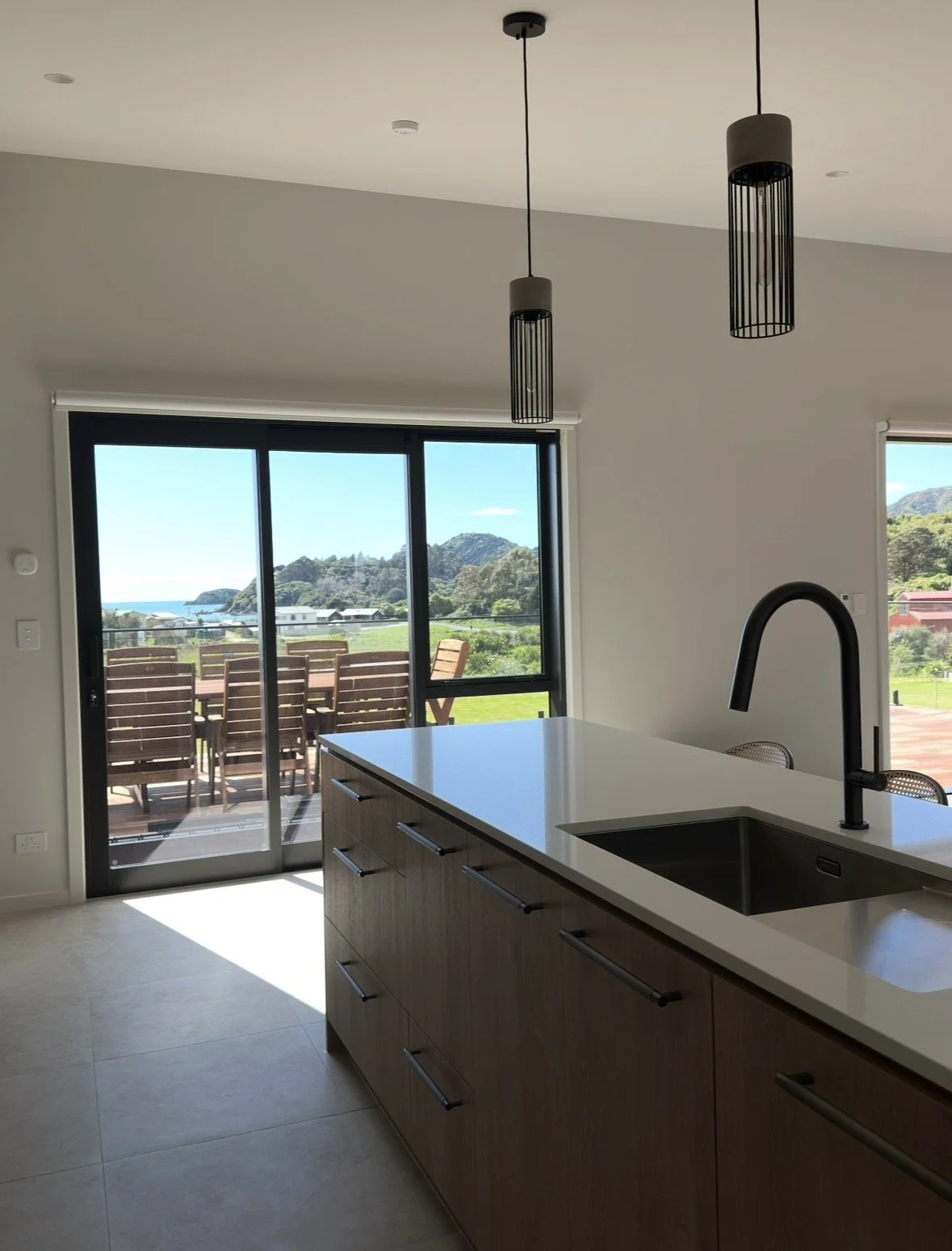 Modern kitchen with island, black sink faucet, pendant lights, and ocean and mountain views through glass doors