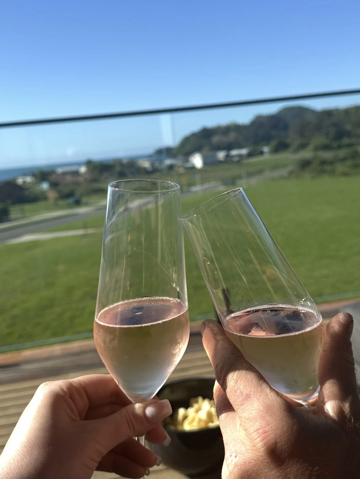 Two people clinking glasses of sparkling rosé wine overlooking a green coastal landscape