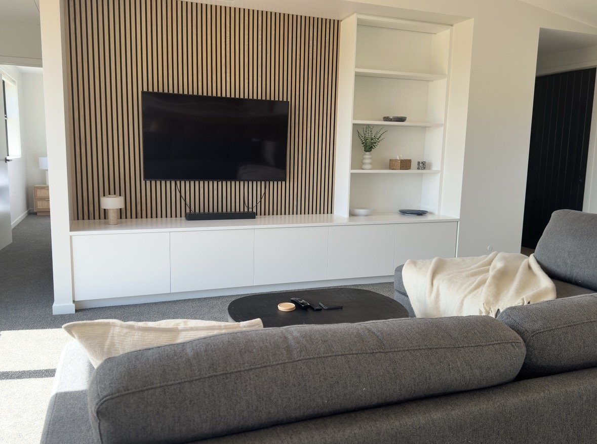 Modern living room with wall-mounted TV, vertical wood-slat accent wall, white built-in cabinets, gray sectional sofa, and black coffee table