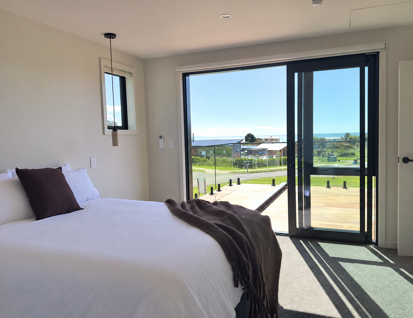 Bright bedroom with a neatly made bed, ocean-view balcony, and sliding glass doors opening to a wooden deck