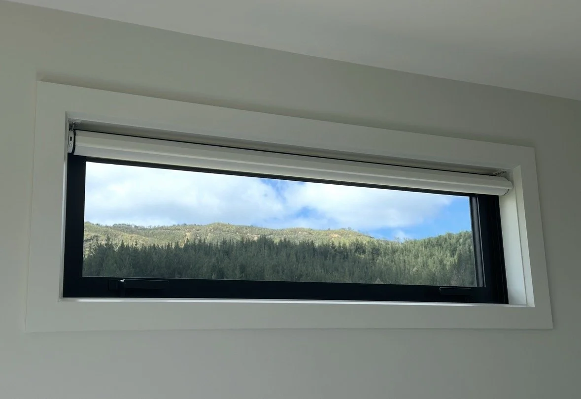 White-framed window overlooking a forested mountain ridge beneath a blue sky