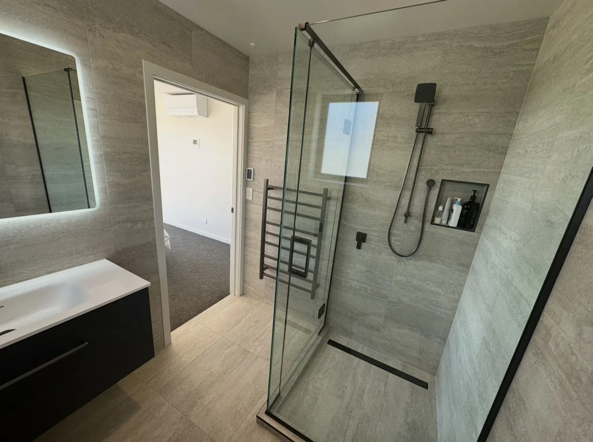 Modern bathroom with a glass-enclosed walk-in shower, wall-mounted fixtures, black vanity, and illuminated mirror
