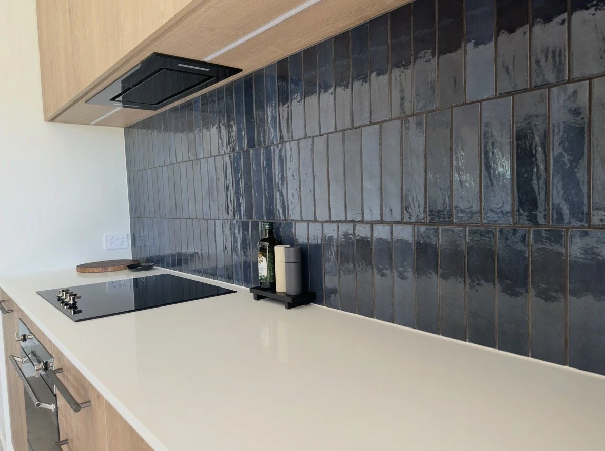 Modern kitchen with glossy dark blue tile backsplash, white countertop, black induction cooktop, and wooden cabinetry