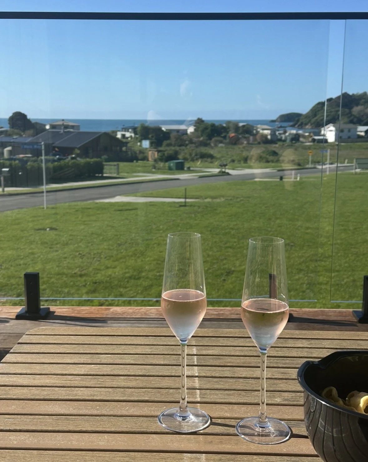 Two glasses of rosé wine on a wooden deck overlooking a coastal neighborhood and ocean