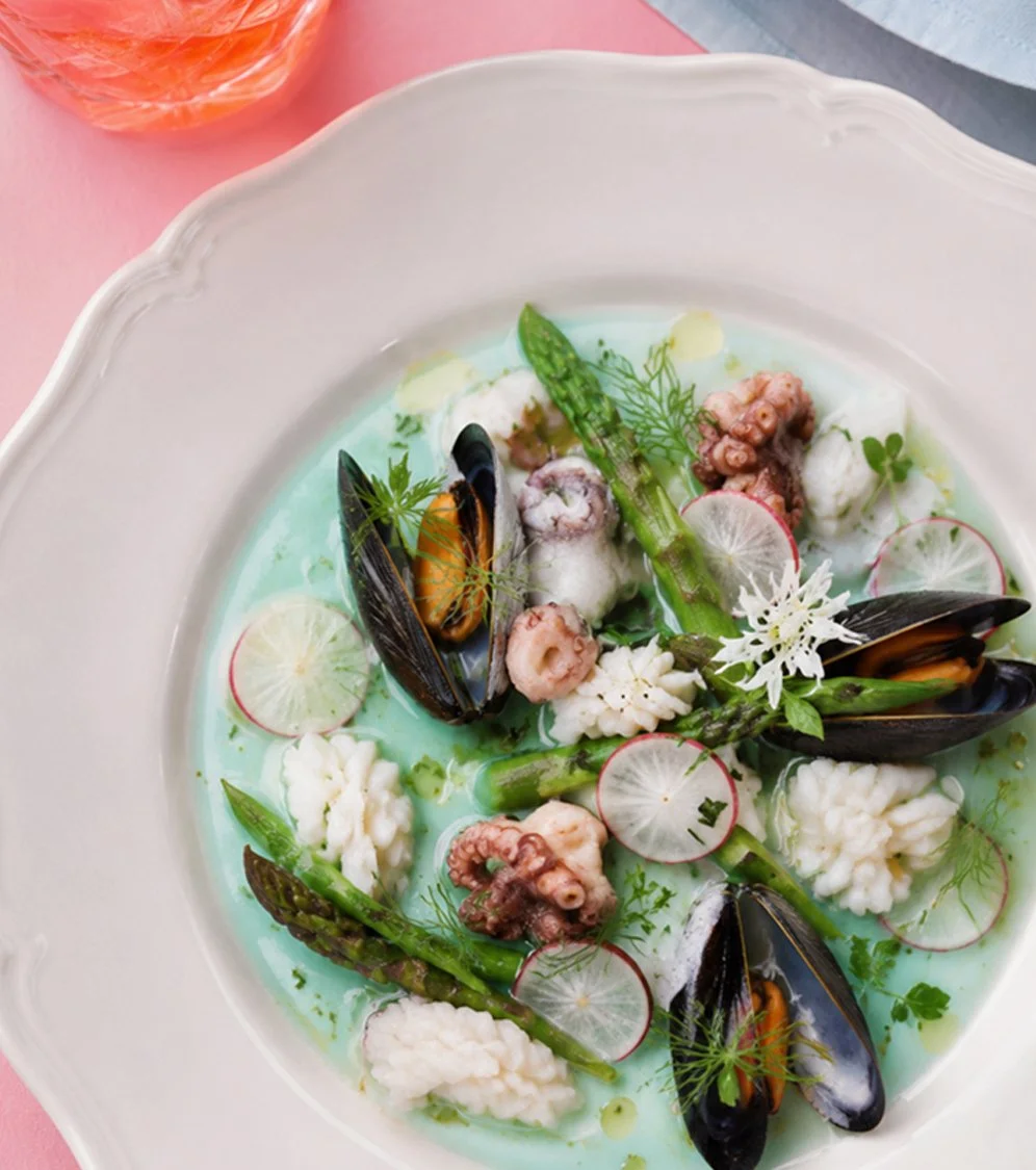 Gourmet seafood plate with mussels, octopus, asparagus, radishes, and edible flowers
