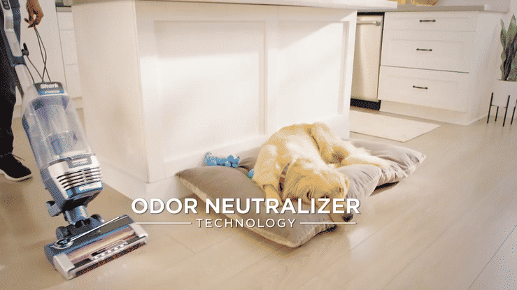 Golden retriever resting on a cushion beside a vacuum cleaner in a bright kitchen with odor neutralizer technology text