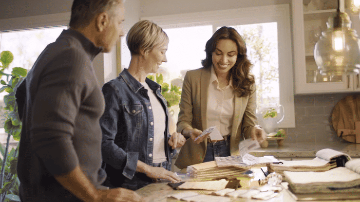Three people reviewing documents and plans at a kitchen counter