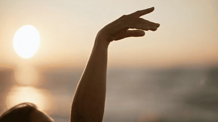 Silhouetted raised hand against a glowing sunset over the water