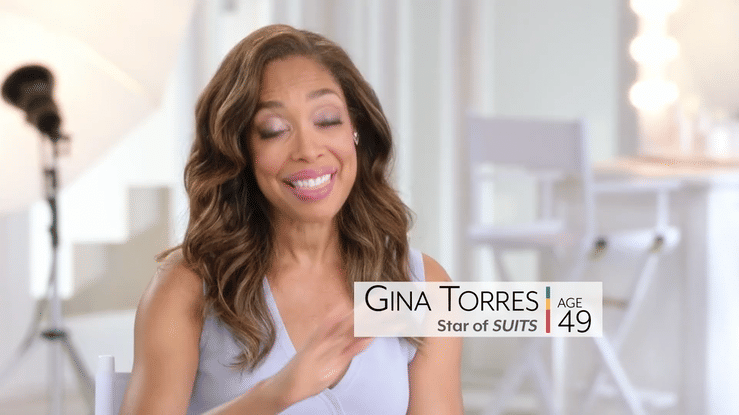 Gina Torres, star of Suits, smiling in an interview with an on-screen age label of 49