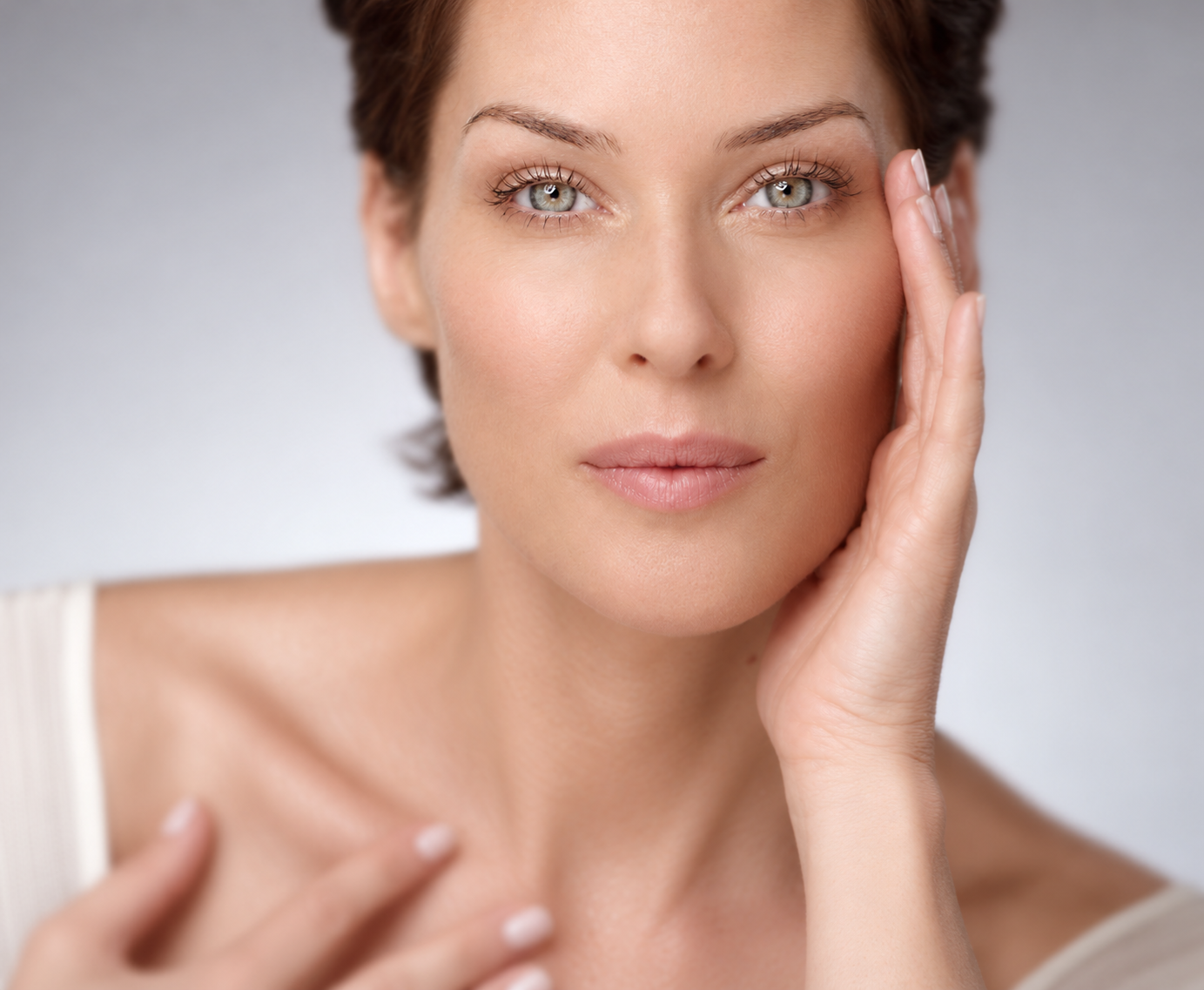 Close-up portrait of a woman touching her cheek and collarbone, highlighting smooth, healthy-looking skin.