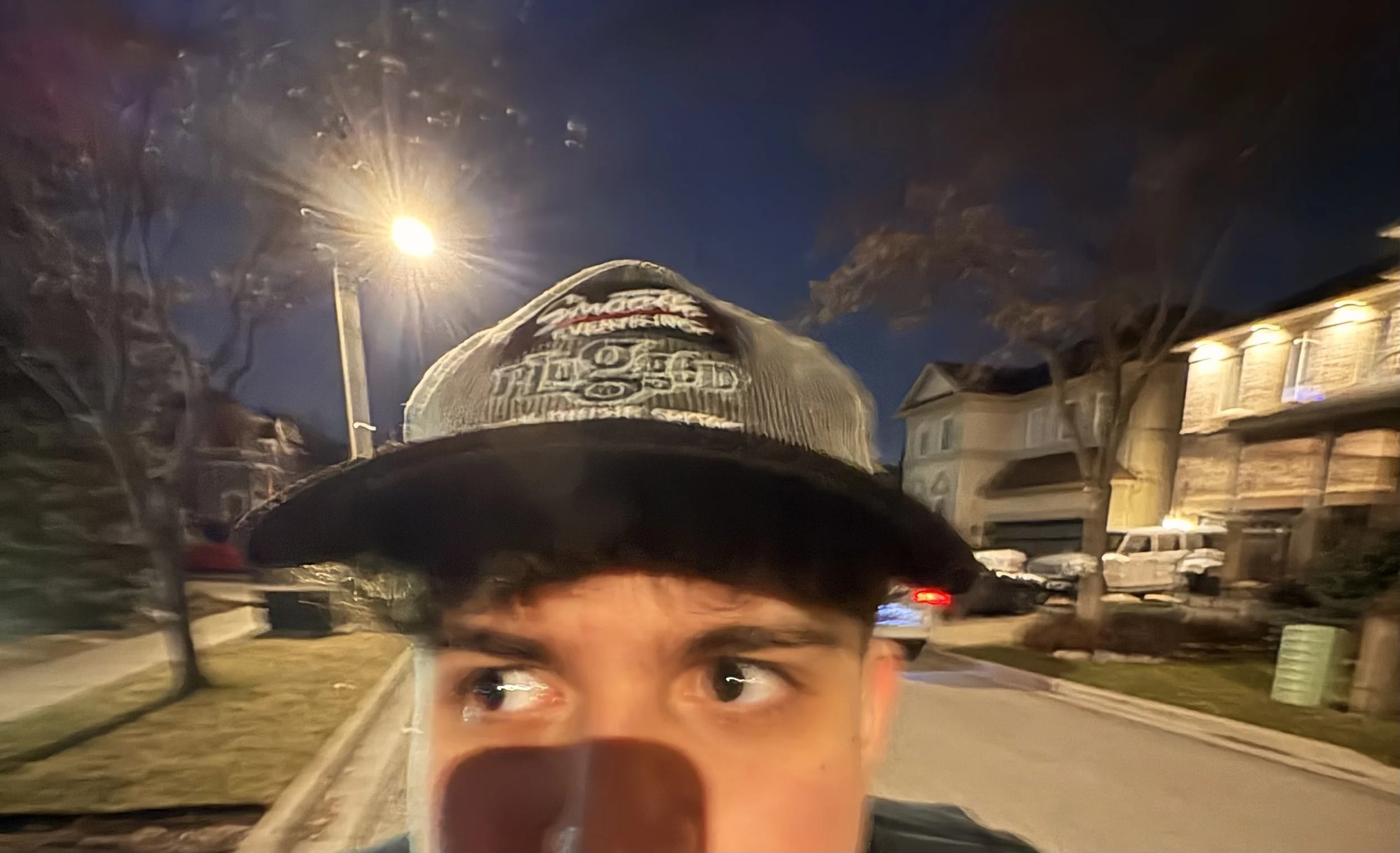 Young man wearing a black embroidered cap takes a nighttime selfie on a residential street.