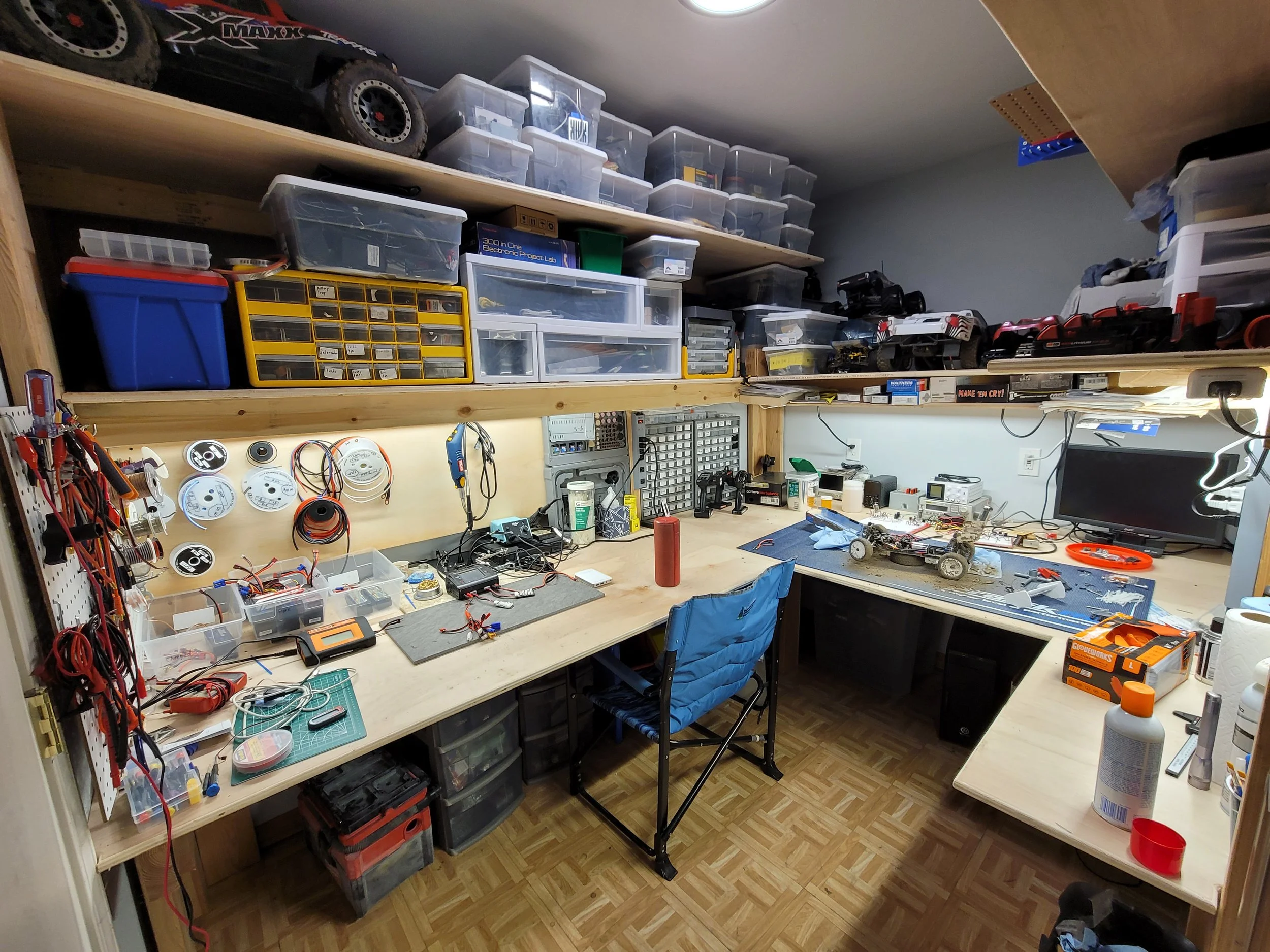 Electronics and remote-control car workshop with organized shelves, tools, circuit components, wires, and workbenches.