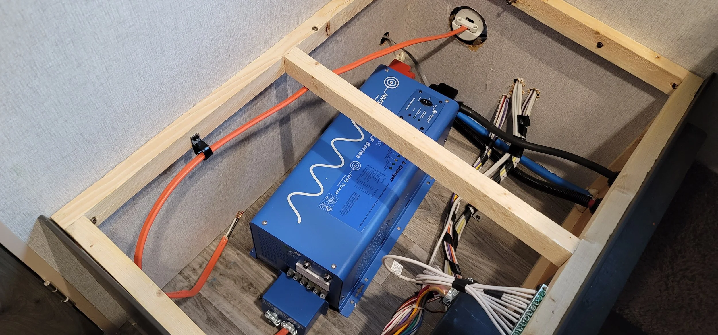 Victron Energy electrical power system with blue inverter, wiring, orange power cable, and wooden framing inside a compartment