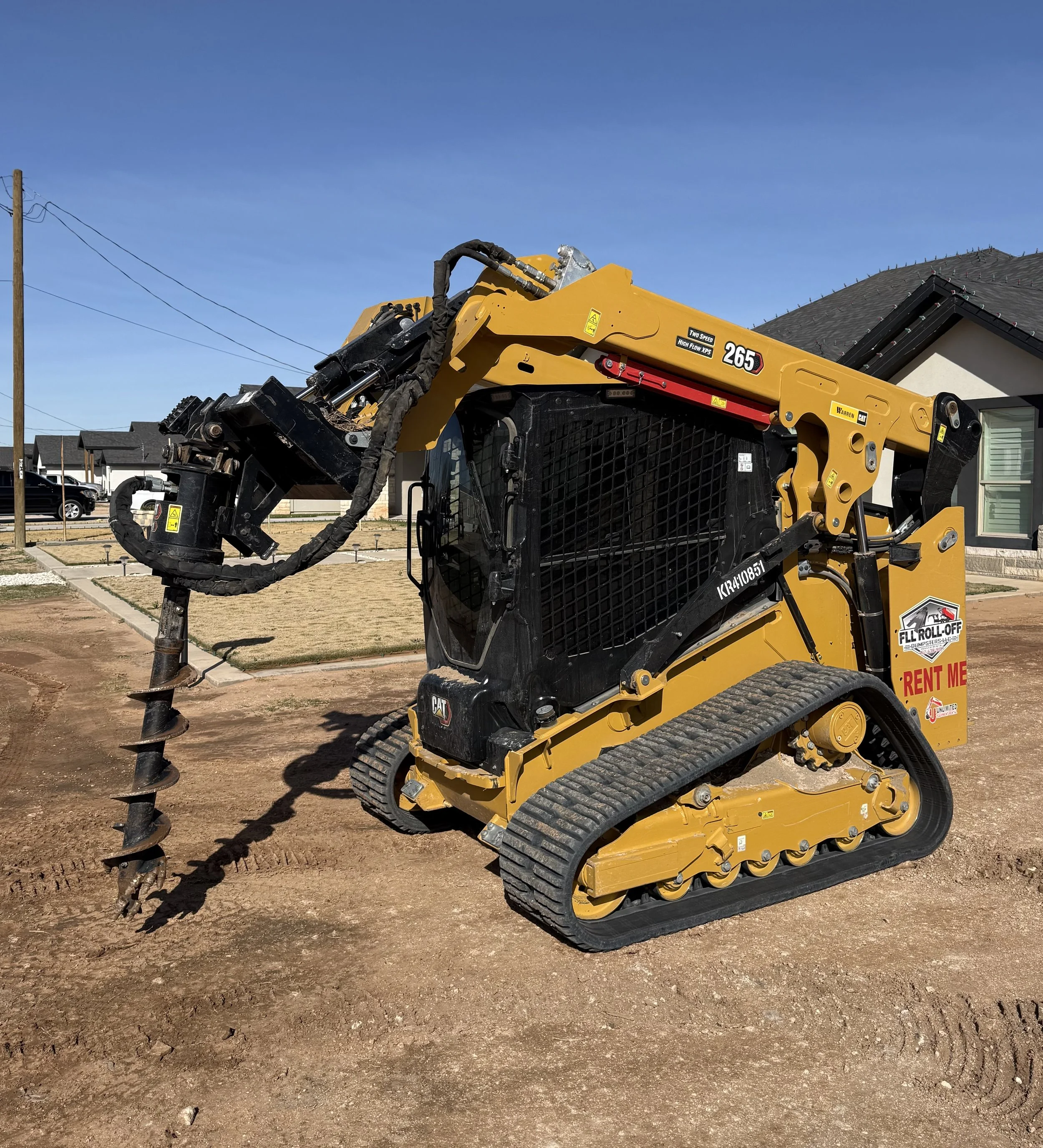 Yellow tracked CAT 265 compact track loader with auger attachment at a residential construction site