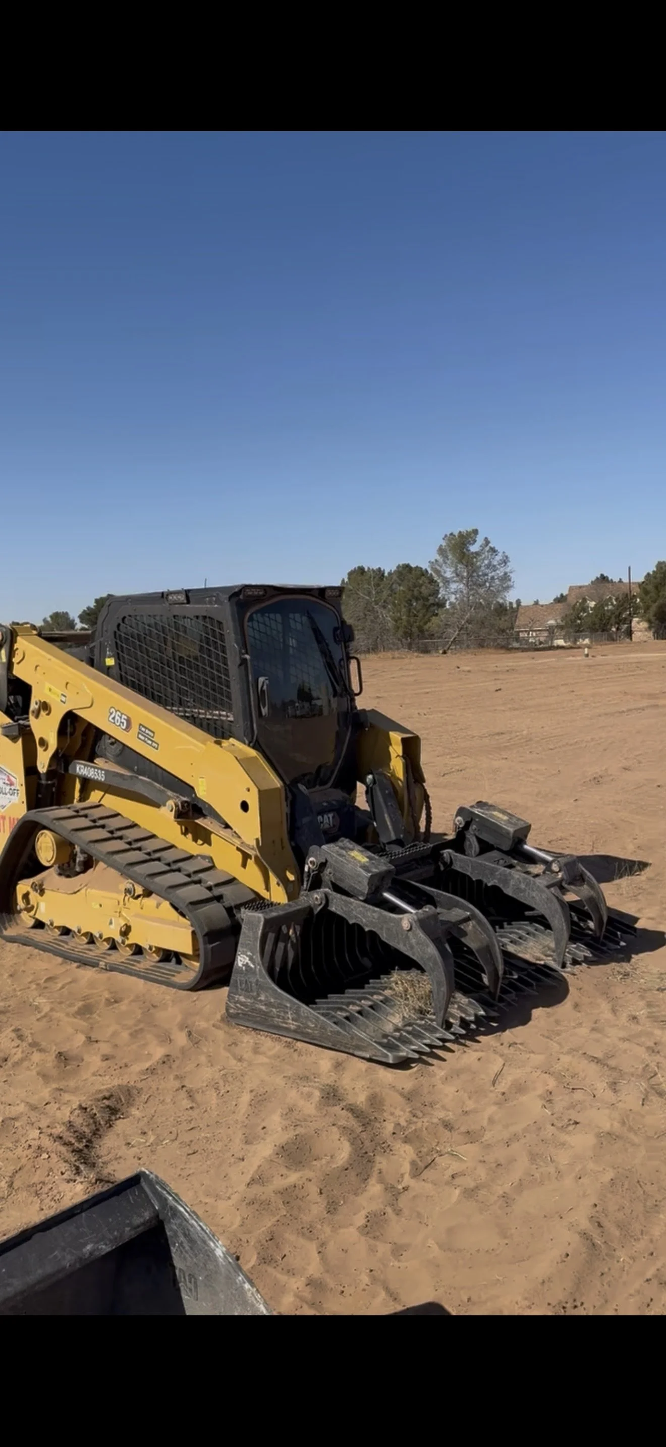 Yellow CAT 265 compact track loader with a grapple bucket parked on a dirt construction site.