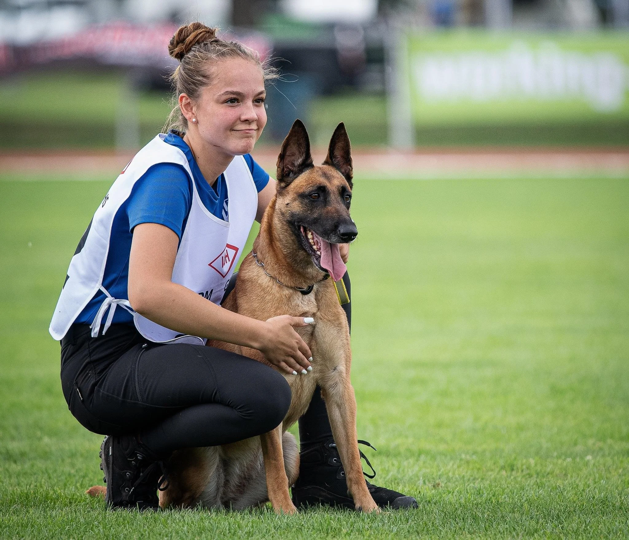 Eine junge Frau trägt einen Deutschen Schäferhund auf einem Sportplatz.