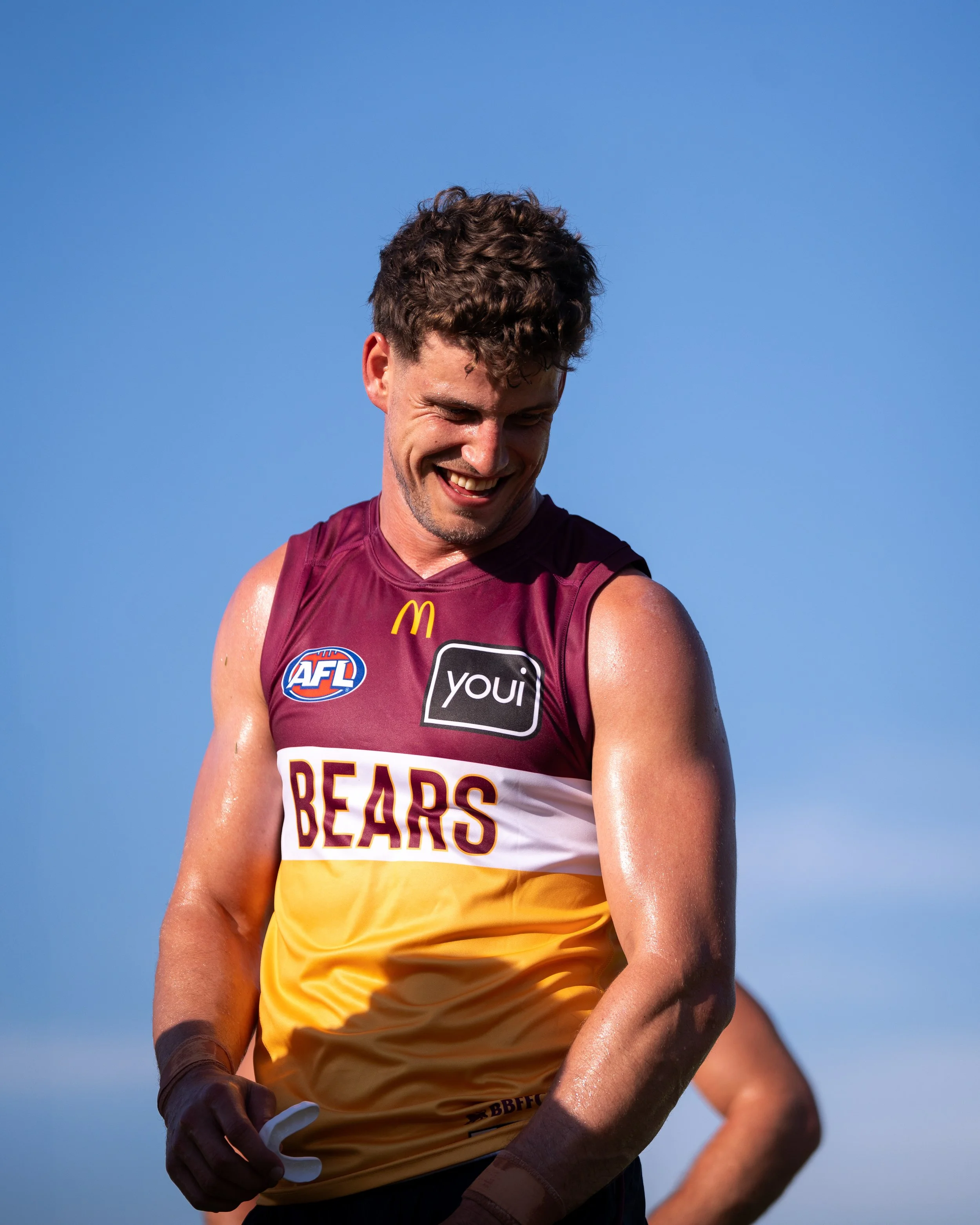Smiling Australian rules football player in a Brisbane Bears jersey against a blue sky