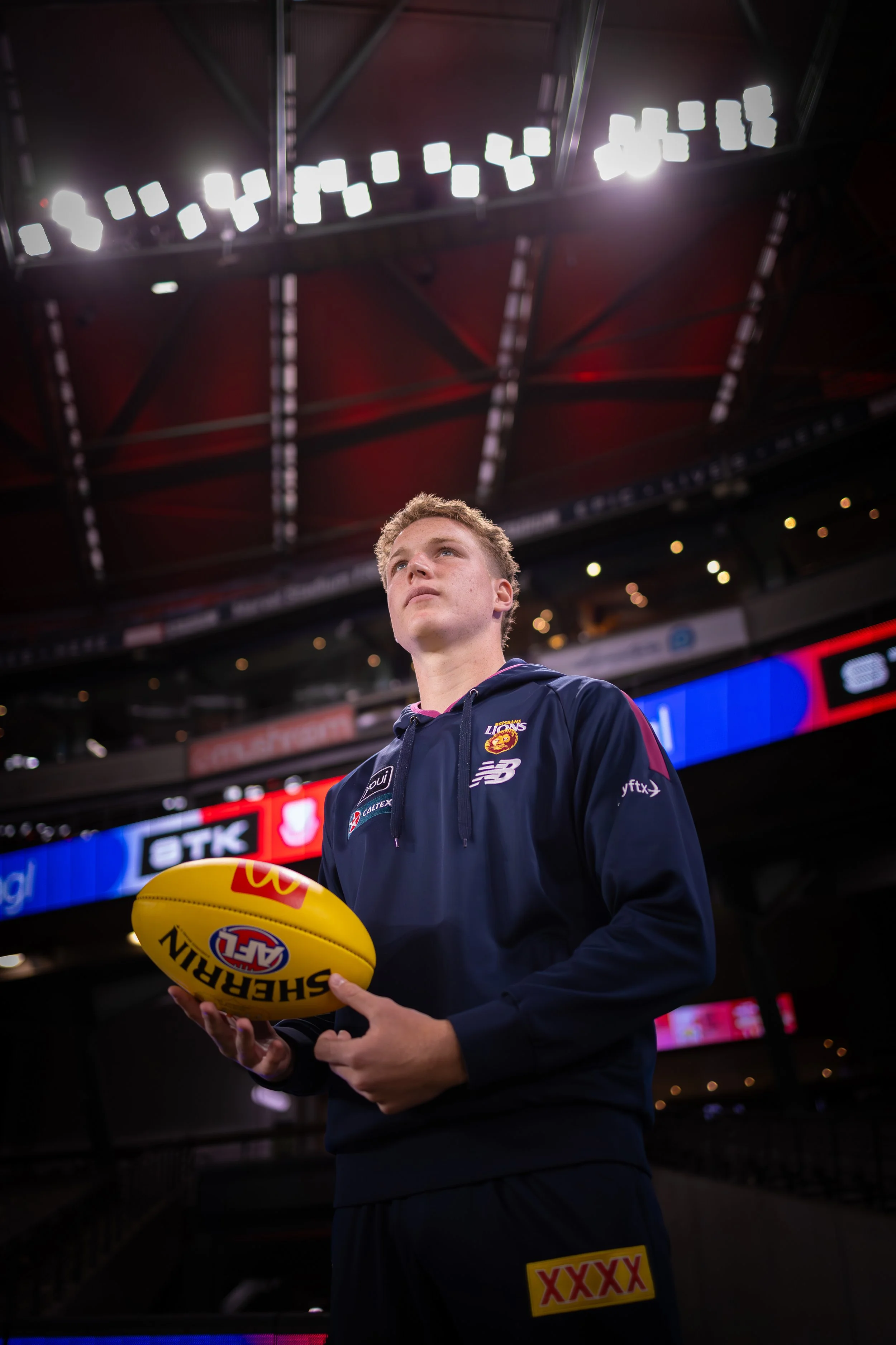 Brisbane Lions player holding a yellow Sherrin football inside a stadium