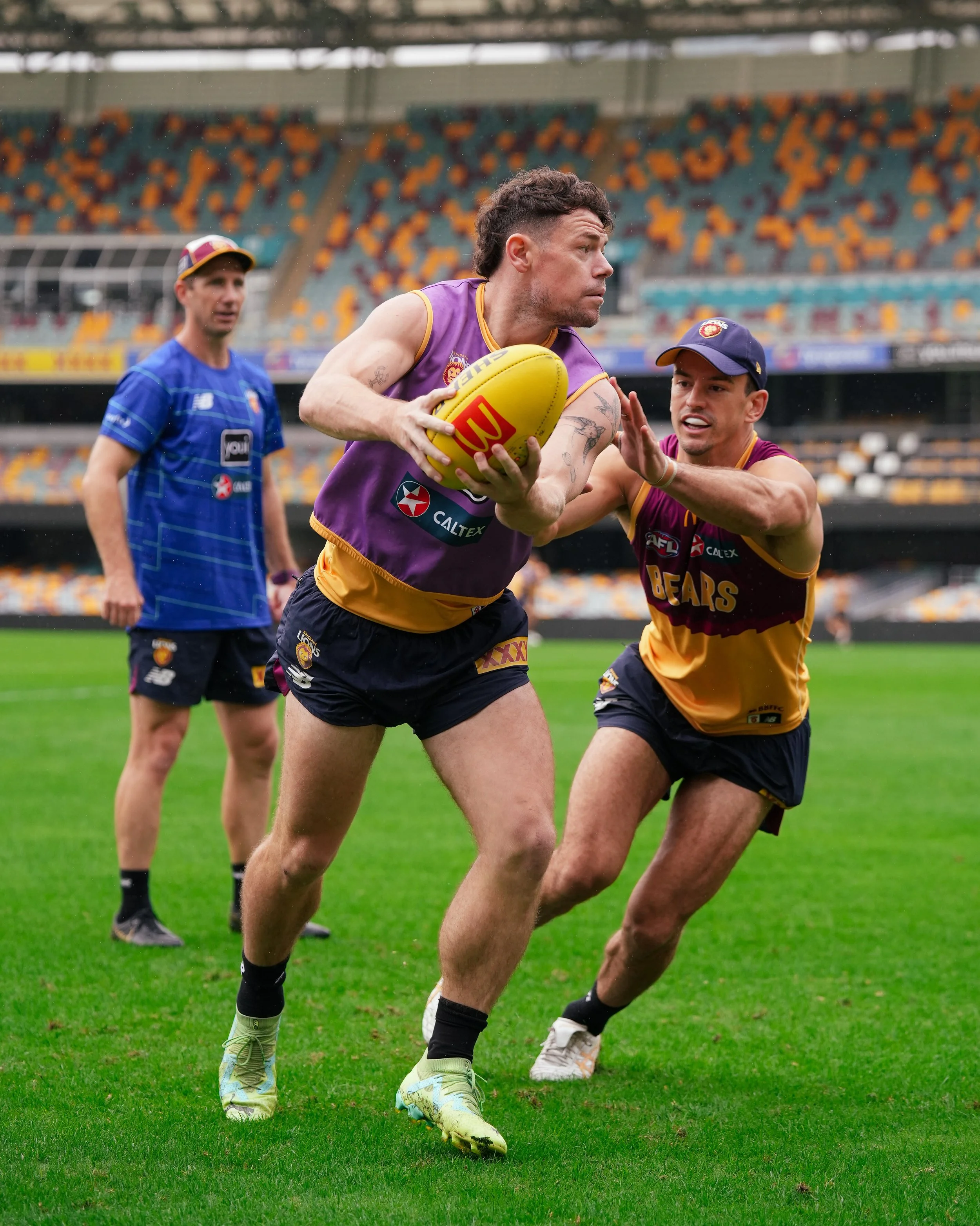 Australian rules football player in a Brisbane Lions jersey carrying the ball during a rainy match