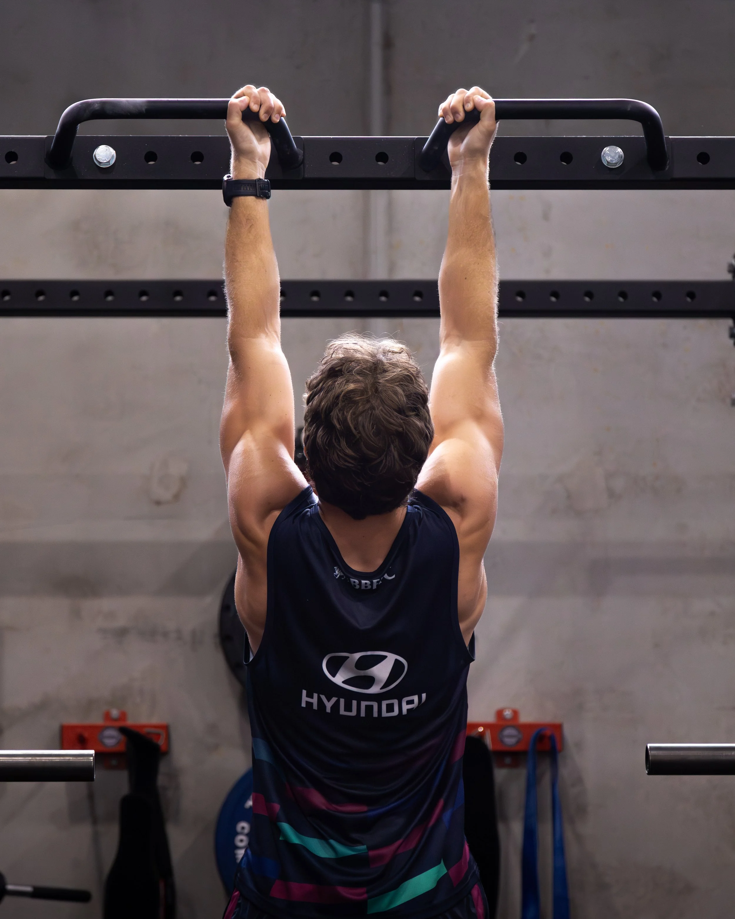 Athlete performing a pull-up on a black gym bar.