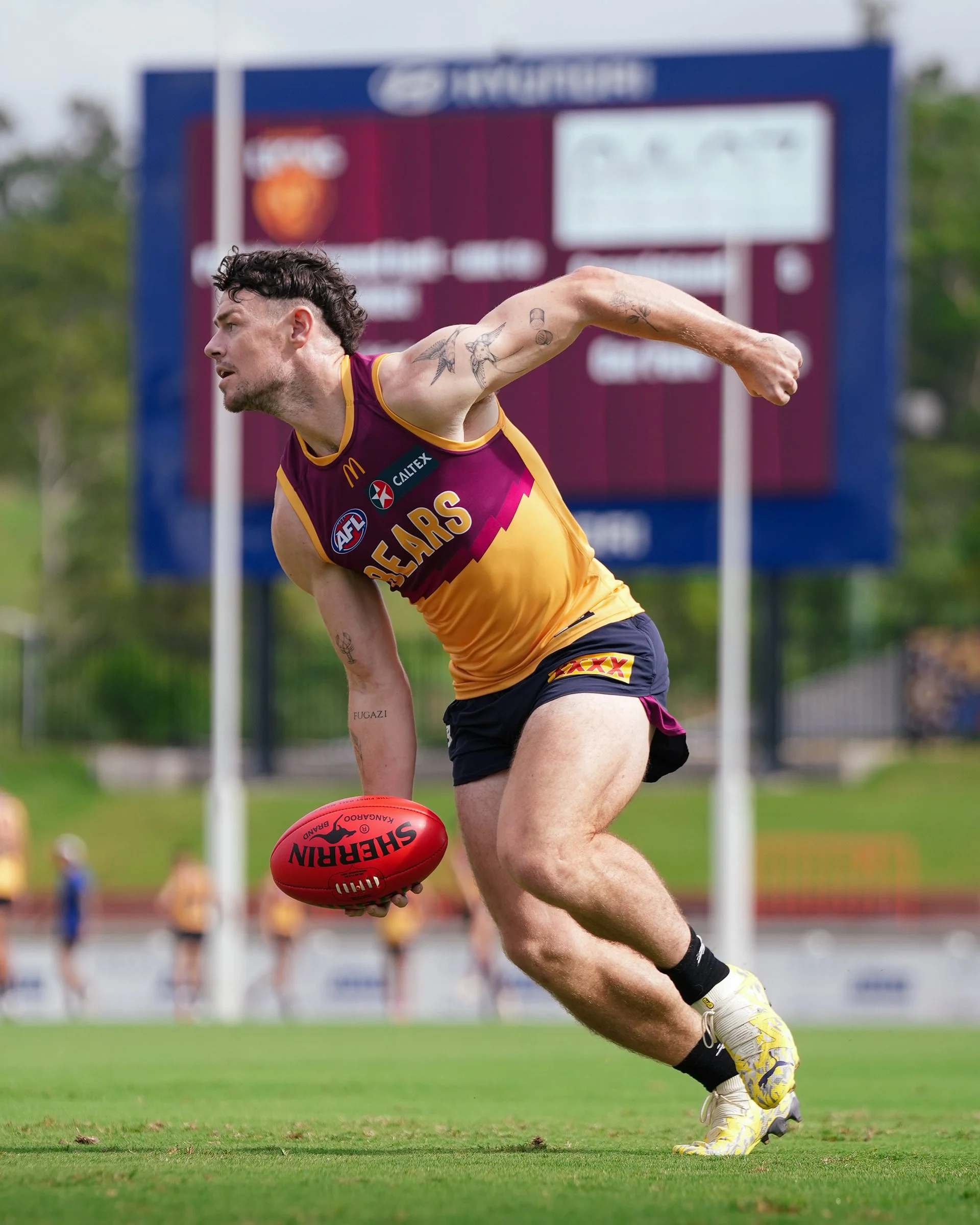 Brisbane Lions Australian rules football player running with a red Sherrin ball during training