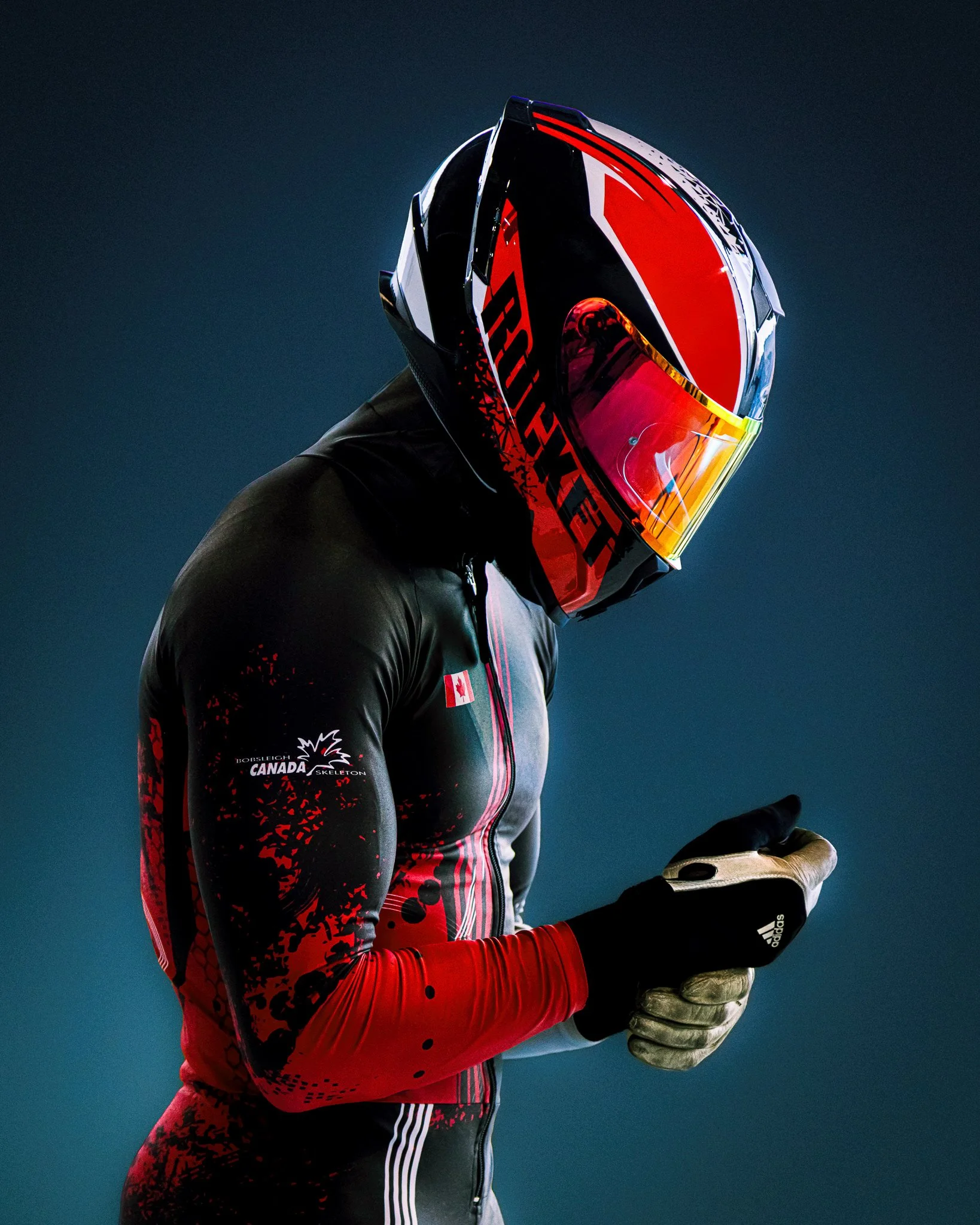 Canadian skeleton racer wearing a red, black, and white helmet and racing suit with gloves