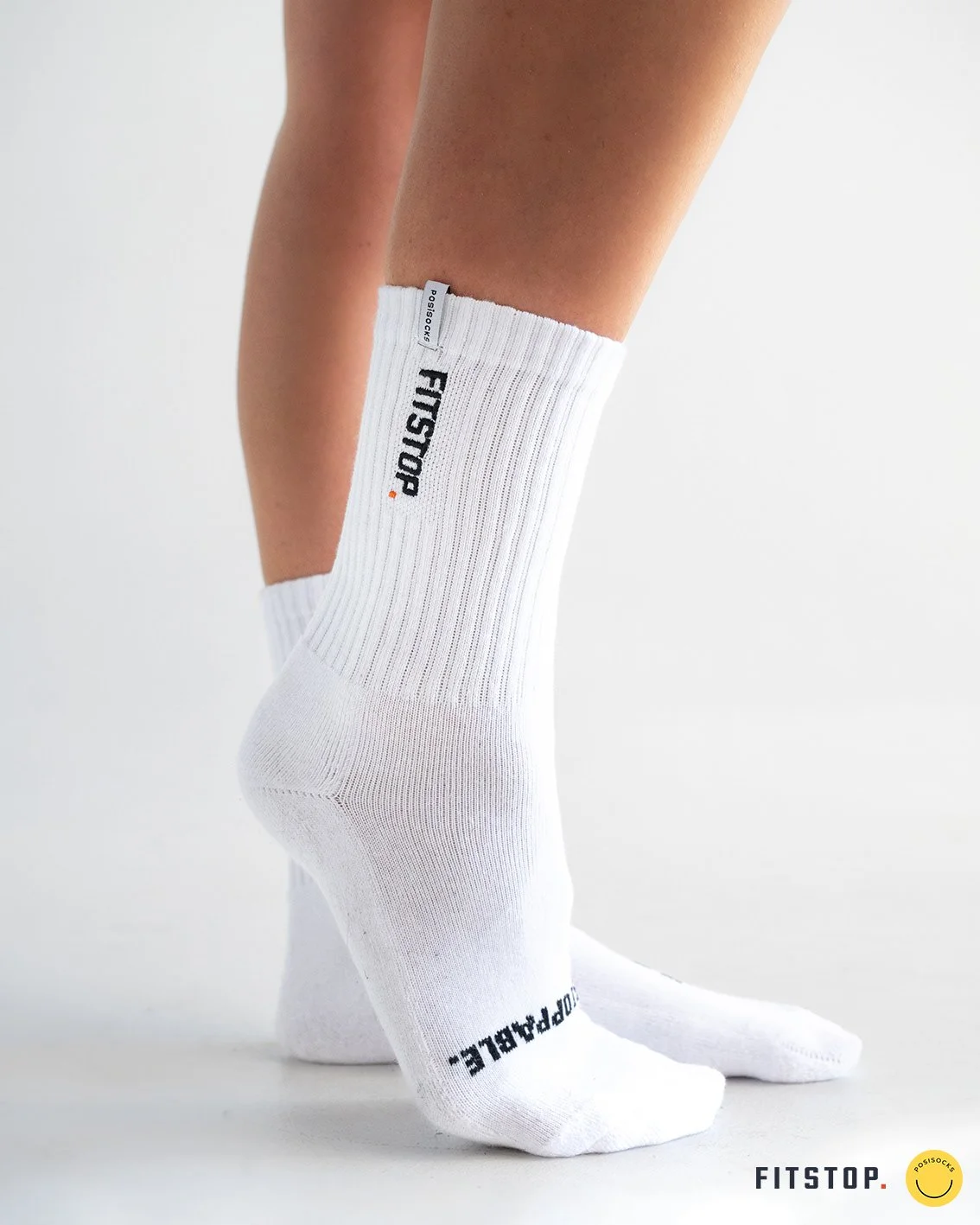 Close-up of white Fitstop crew socks worn on crossed feet, featuring Posistocks branding.