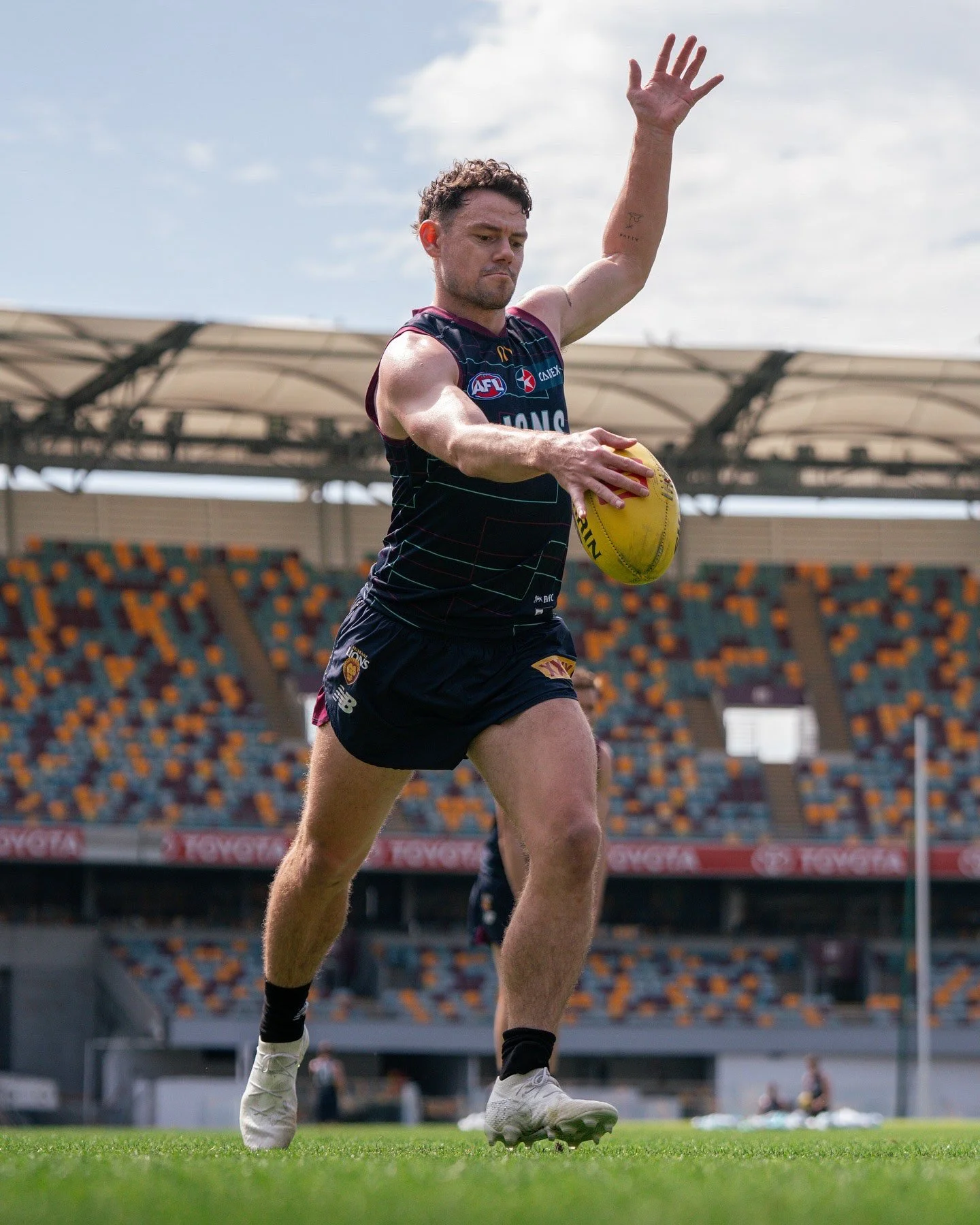 Brisbane Lions Australian rules football player holding a yellow football on the field during training.
