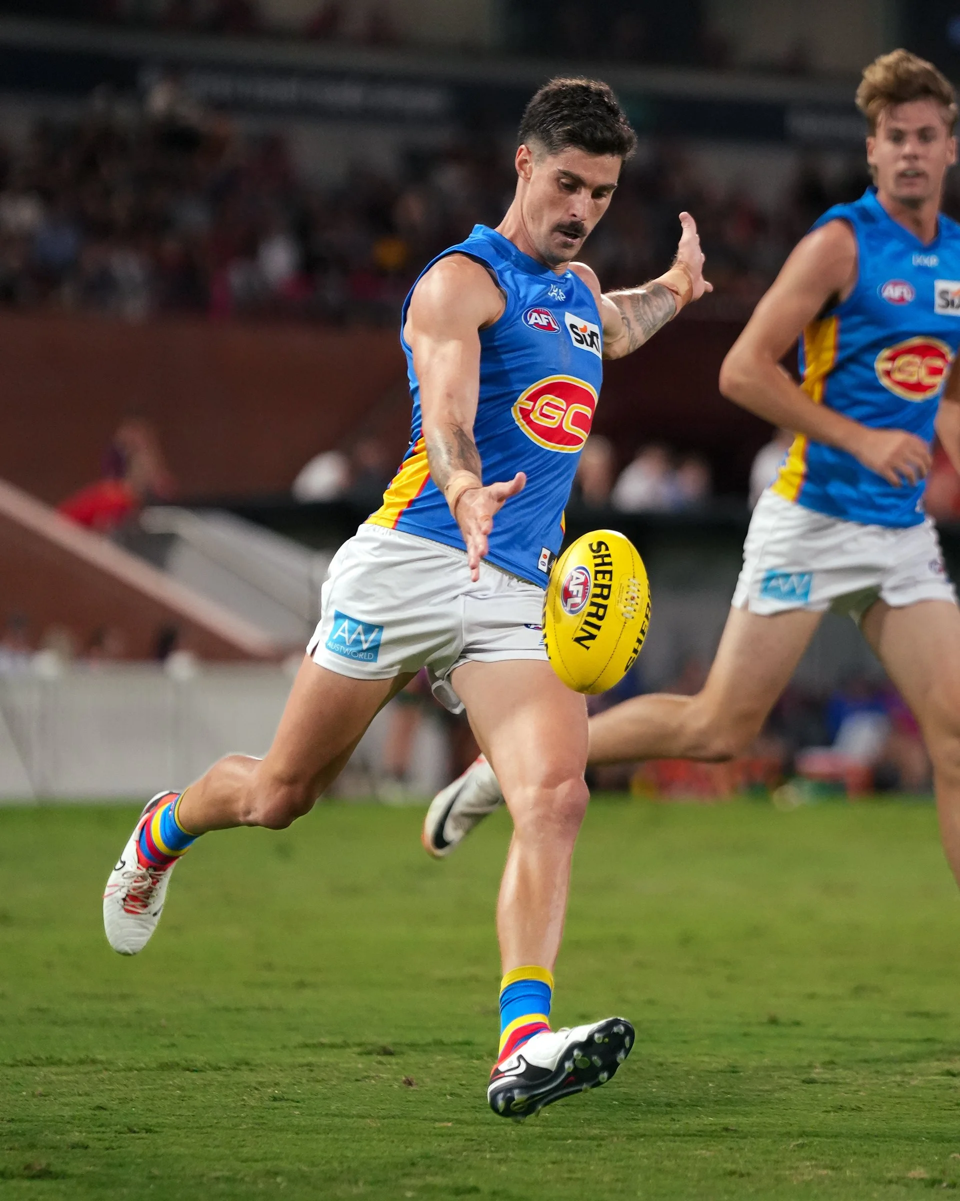 Australian rules football player in a blue and yellow jersey running with an AFL ball during a game