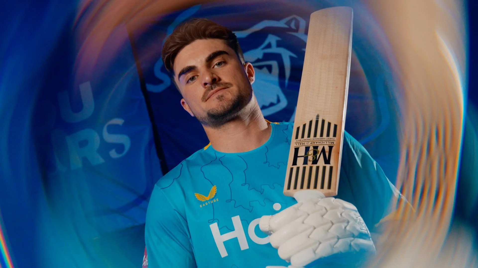 Cricketer in a blue jersey holding a cricket bat and wearing white gloves