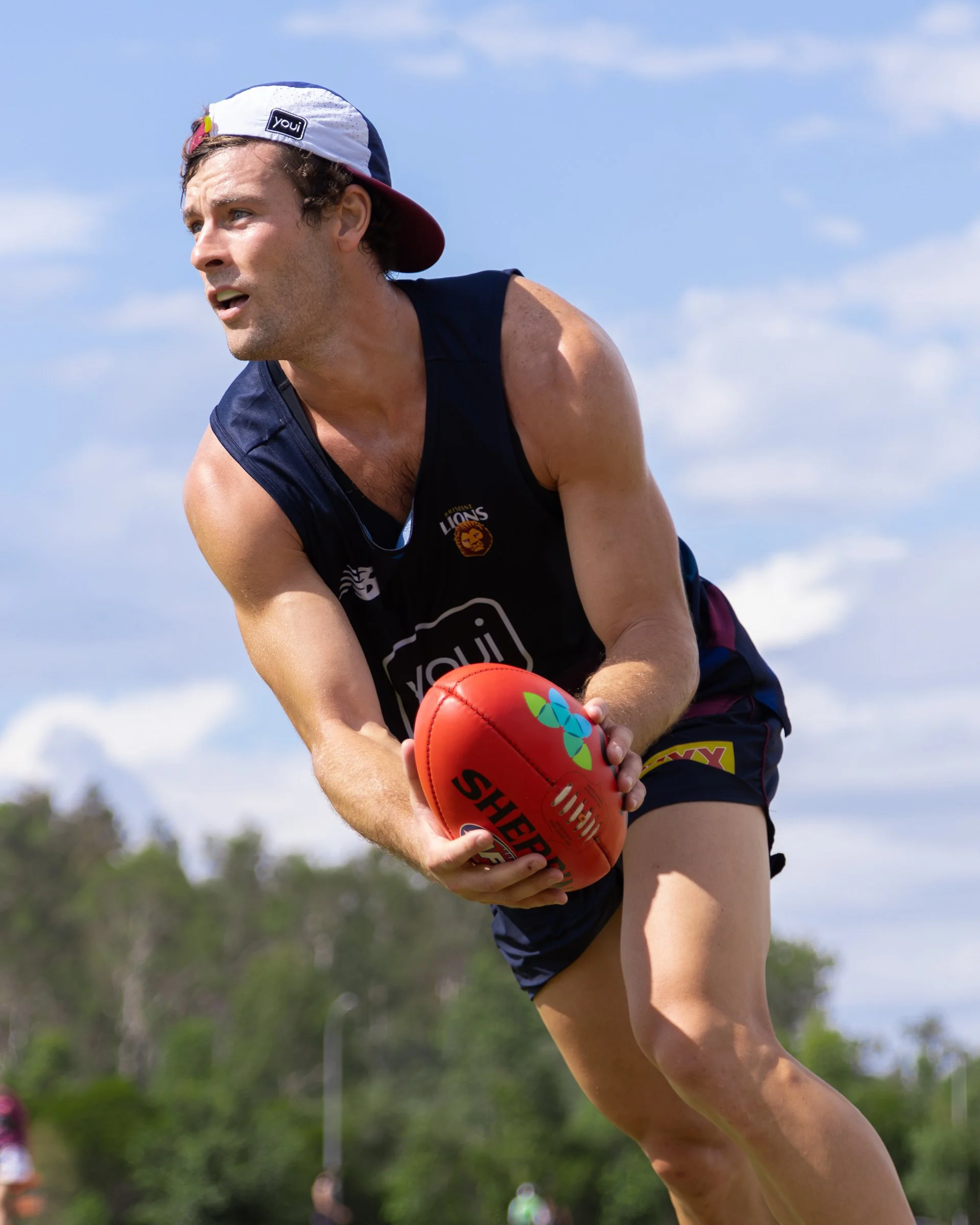 Australian rules football player in a Lions uniform holding a red football outdoors