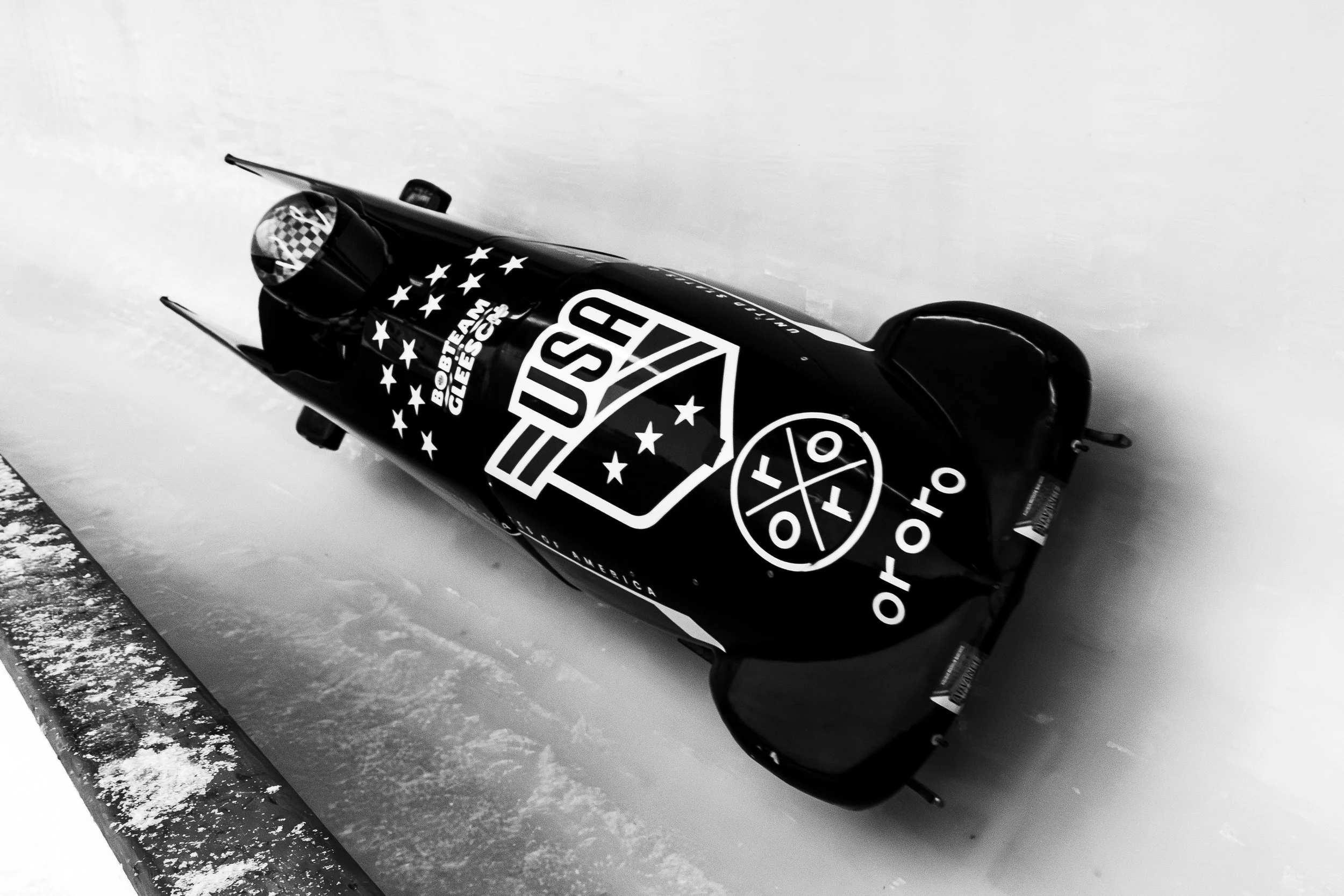 Black bobsled with Stars and Stripes graphics and logos resting on an icy track