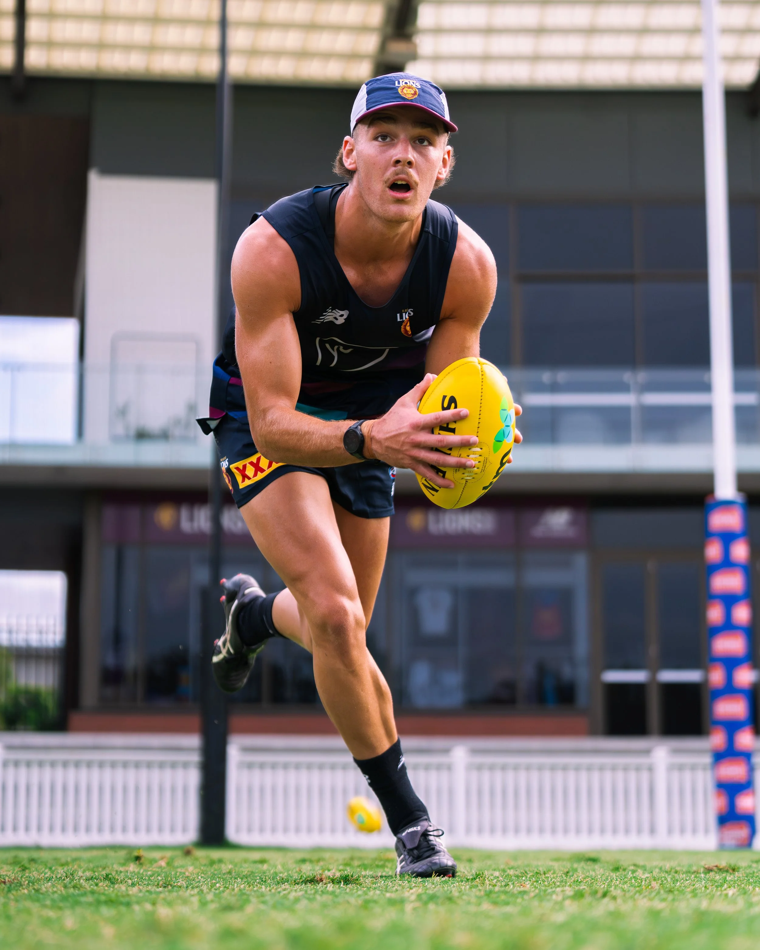 Australian rules football player in Brisbane Lions uniform holding a yellow football during training