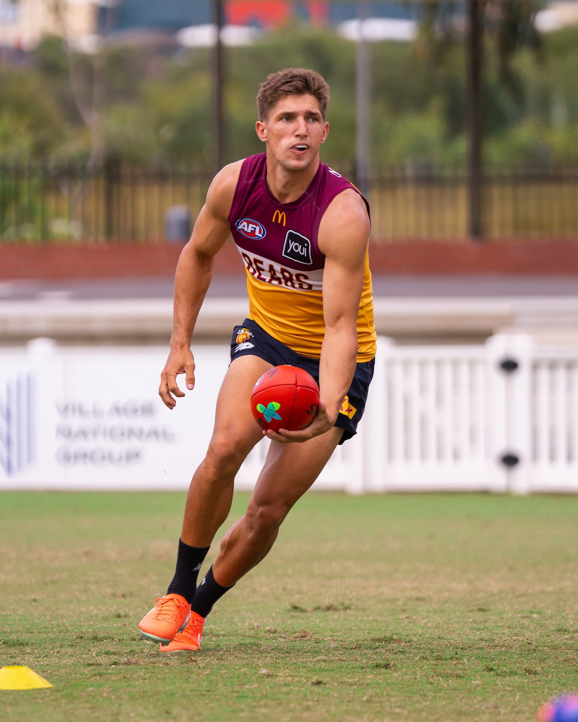 Australian rules football player in a maroon and gold Brisbane Bears jersey running with a red football during training