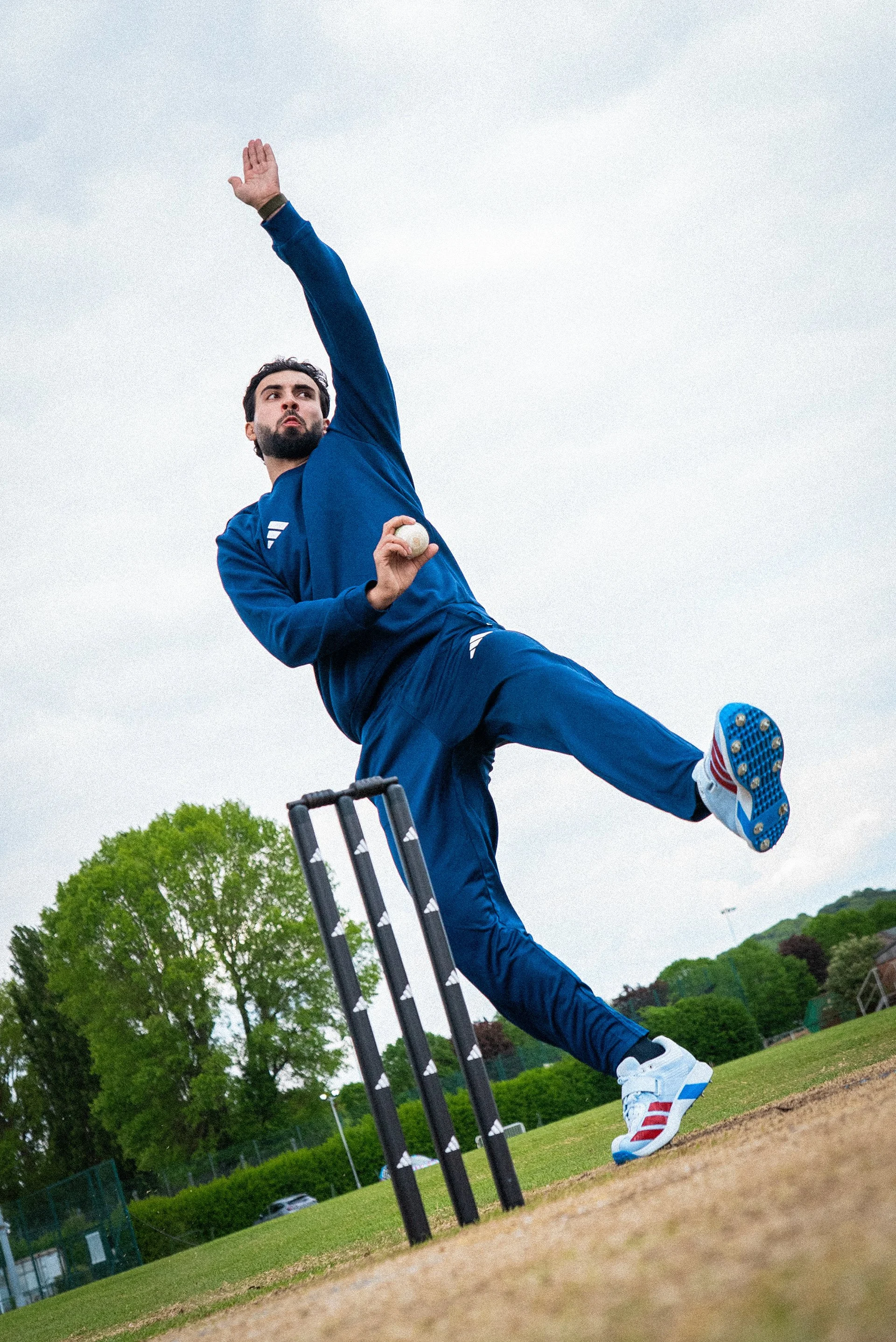 Cricket bowler in blue uniform delivering a ball on a grassy field
