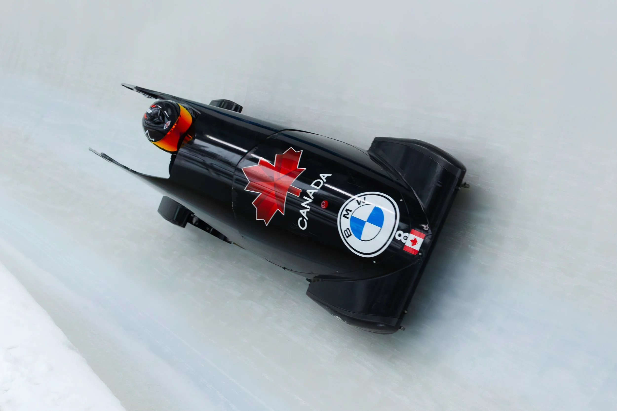 Black Canadian bobsleigh with BMW and Canada team logos racing on an icy track