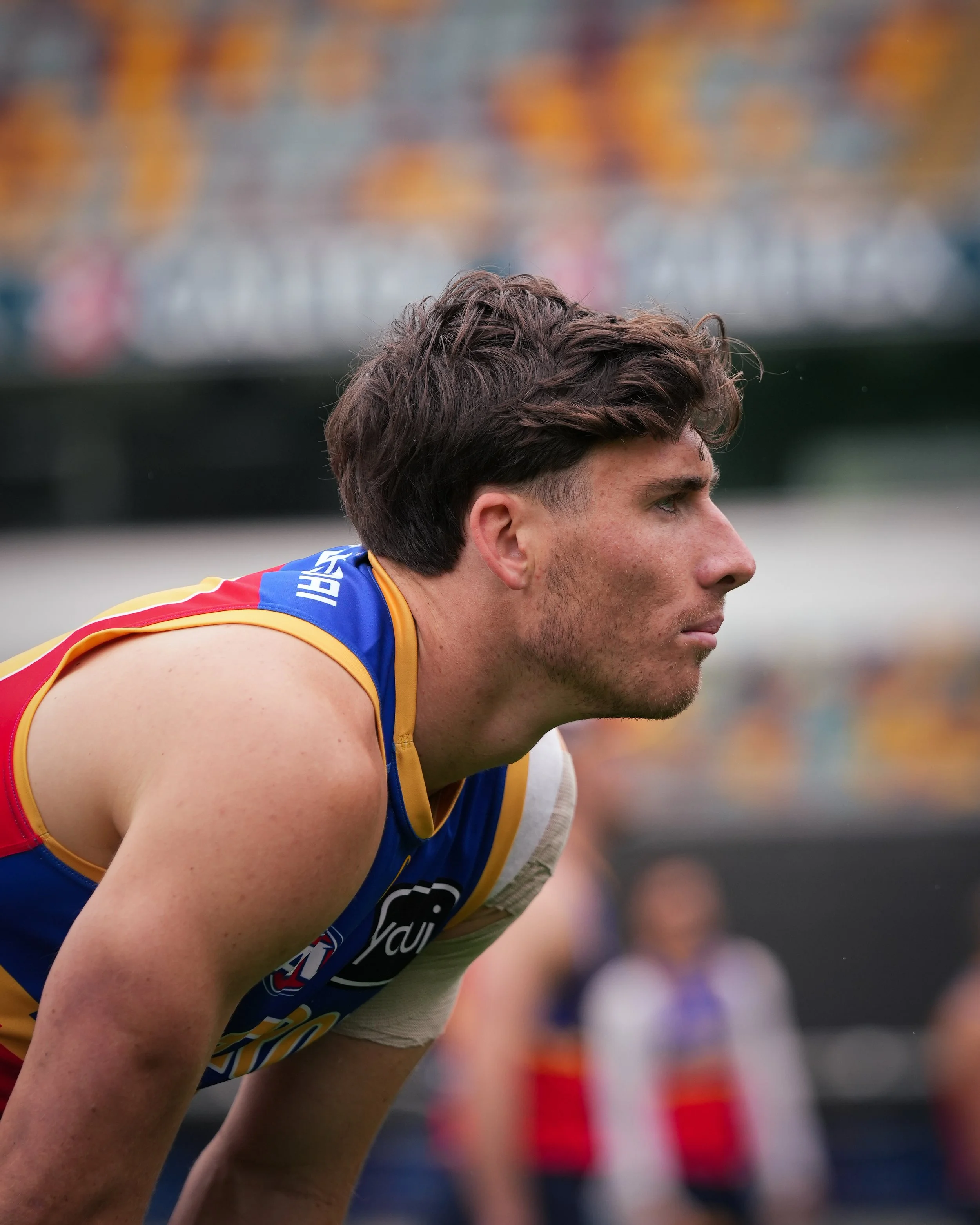 Close-up side profile of a male Australian rules football player in a blue, red, and gold jersey during a game