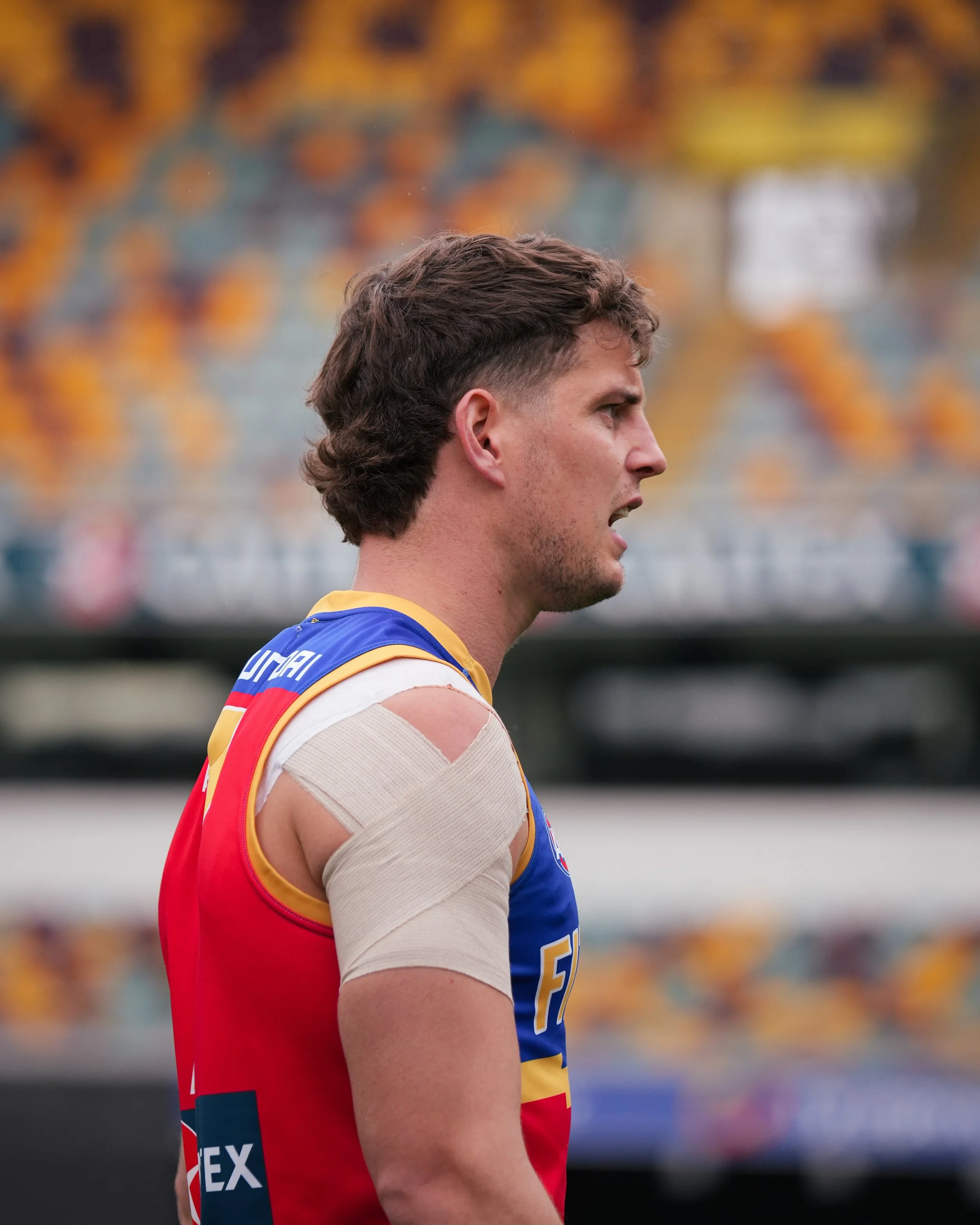 Close-up side profile of a male cyclist wearing a colorful racing jersey and shoulder support tape.