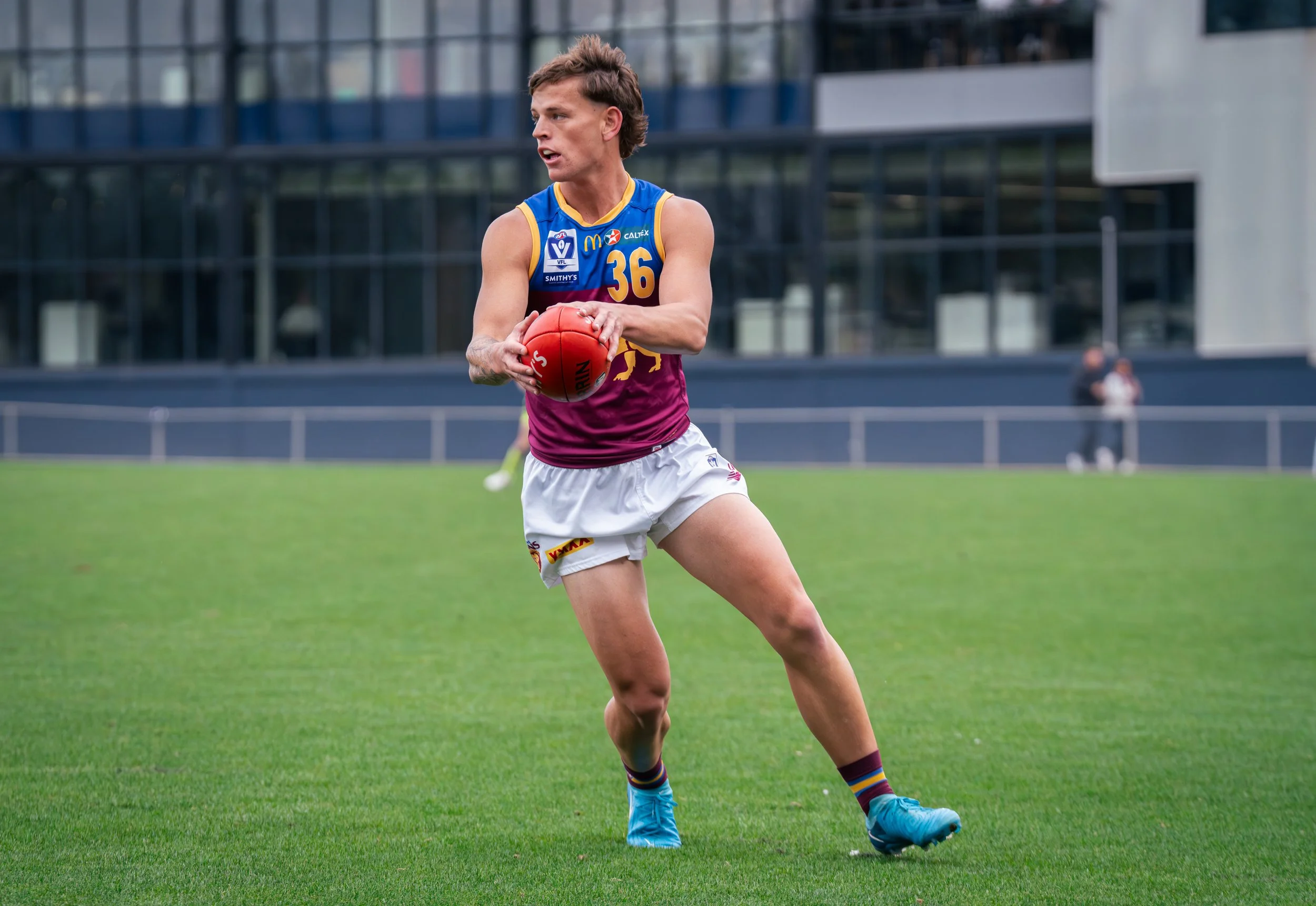 Australian rules football player wearing number 36 jersey holding a red football on a grassy field