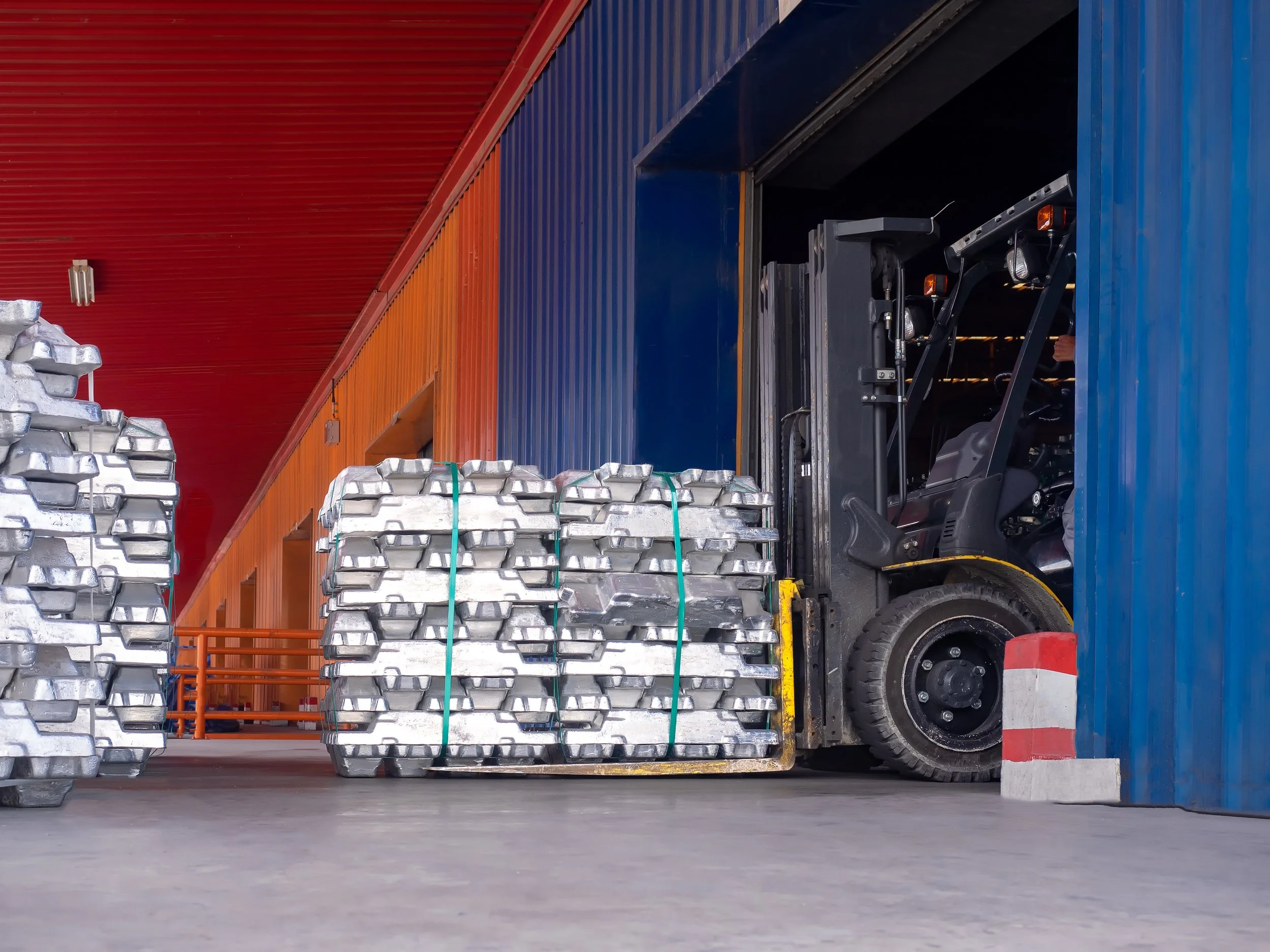 Forklift moving strapped stacks of silver metal ingots inside a colorful industrial warehouse