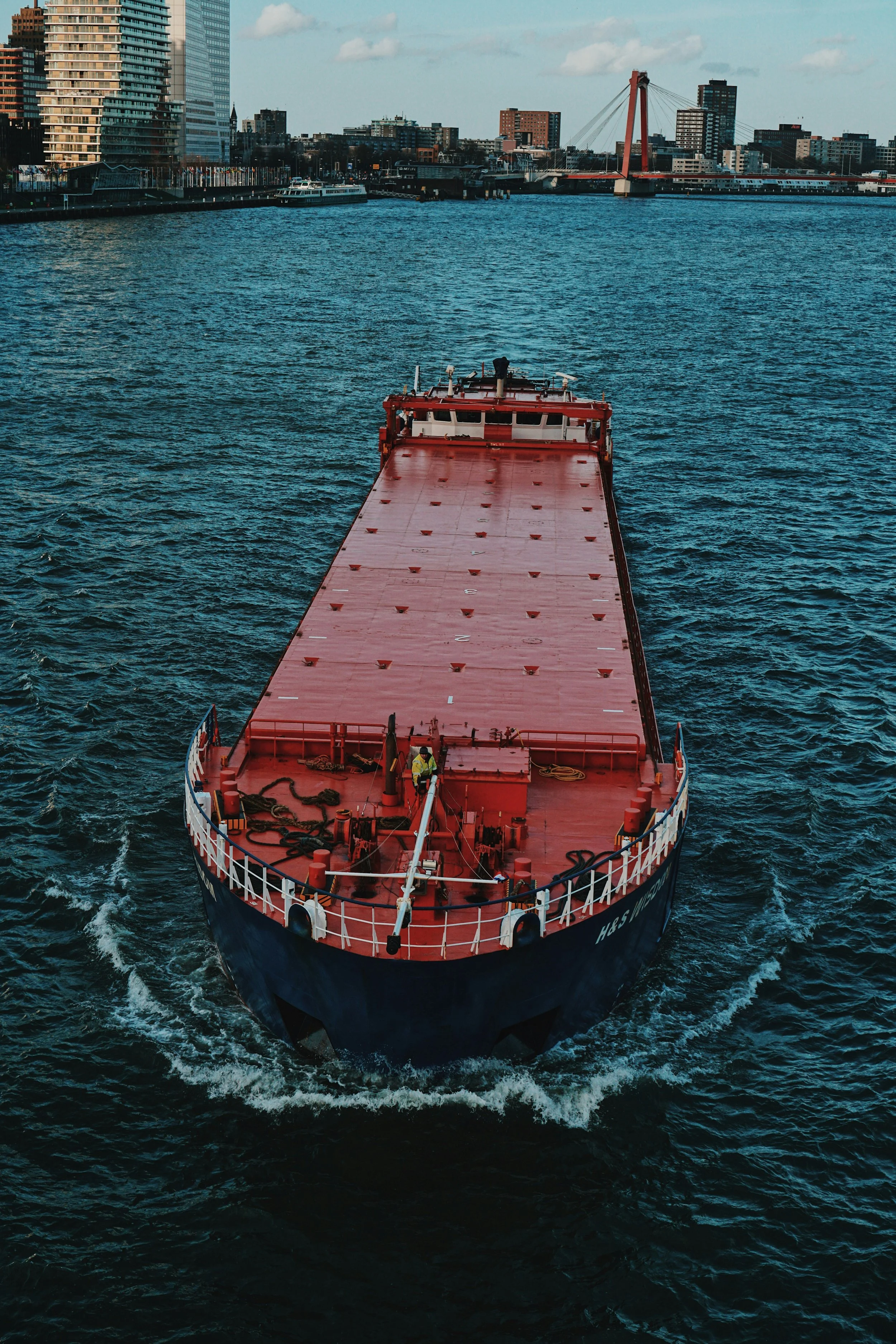 Red cargo ship sailing on a river past Rotterdam’s modern skyline and Erasmus Bridge