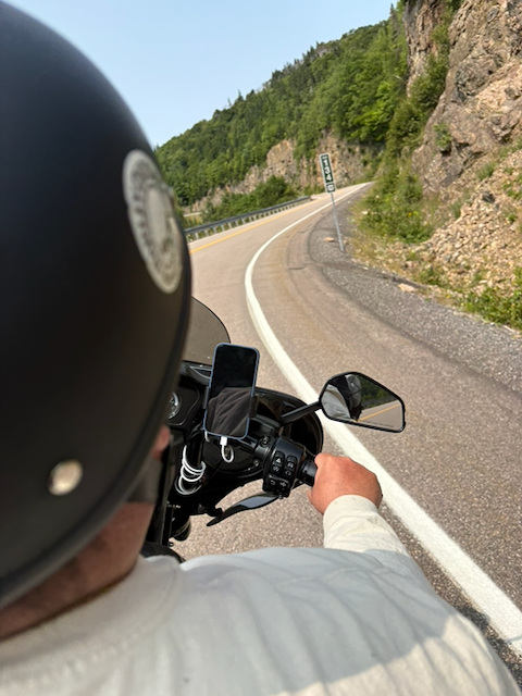 Motorcyclist riding along a winding mountain road beside rocky cliffs and forested hills