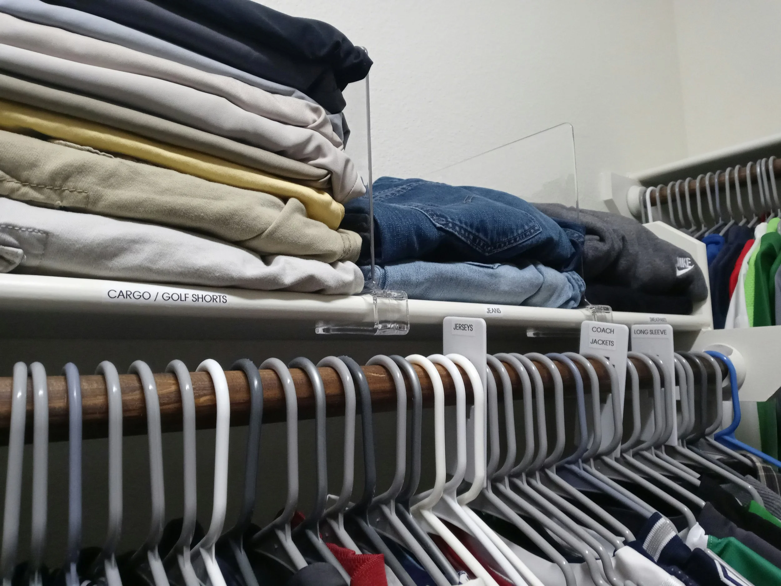 Organized closet with folded clothes, labeled shelves, jeans, jackets, and numerous hangers.