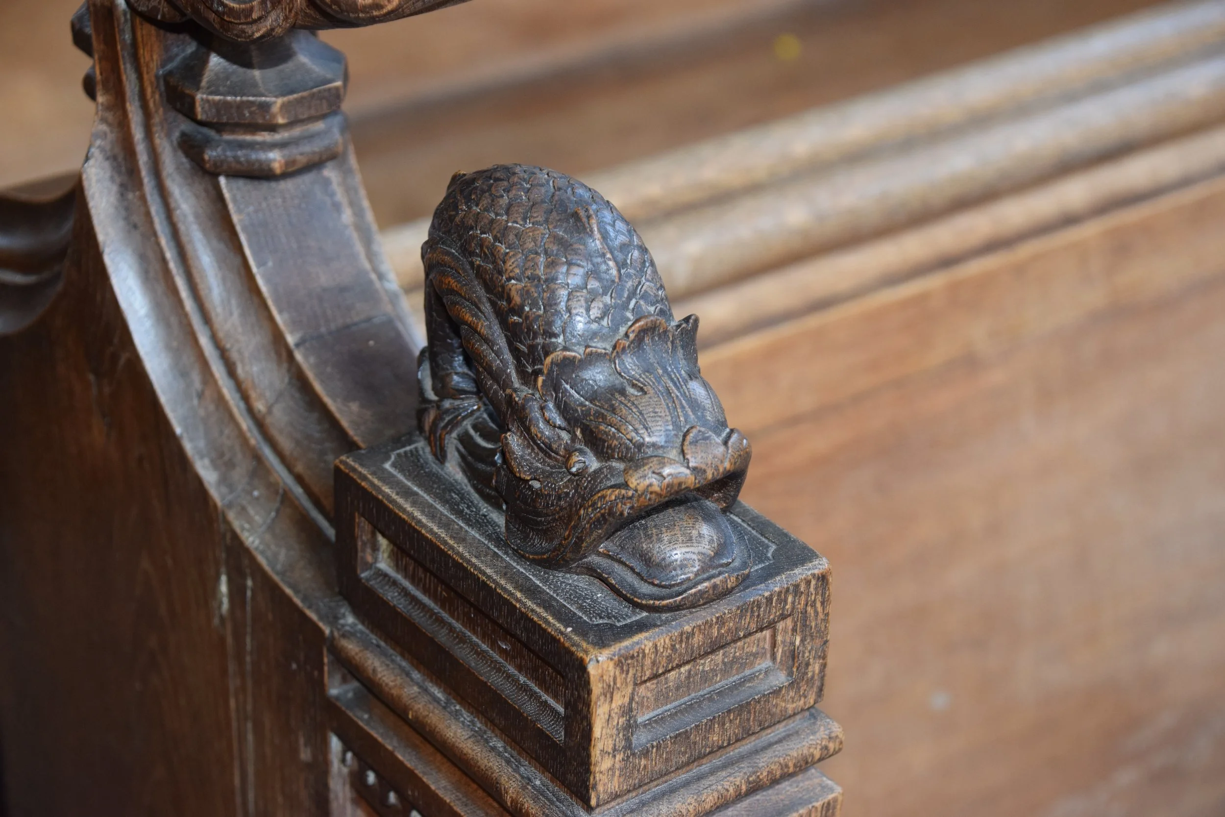 Close-up of an ornate carved wooden dragon finial on a dark antique staircase railing