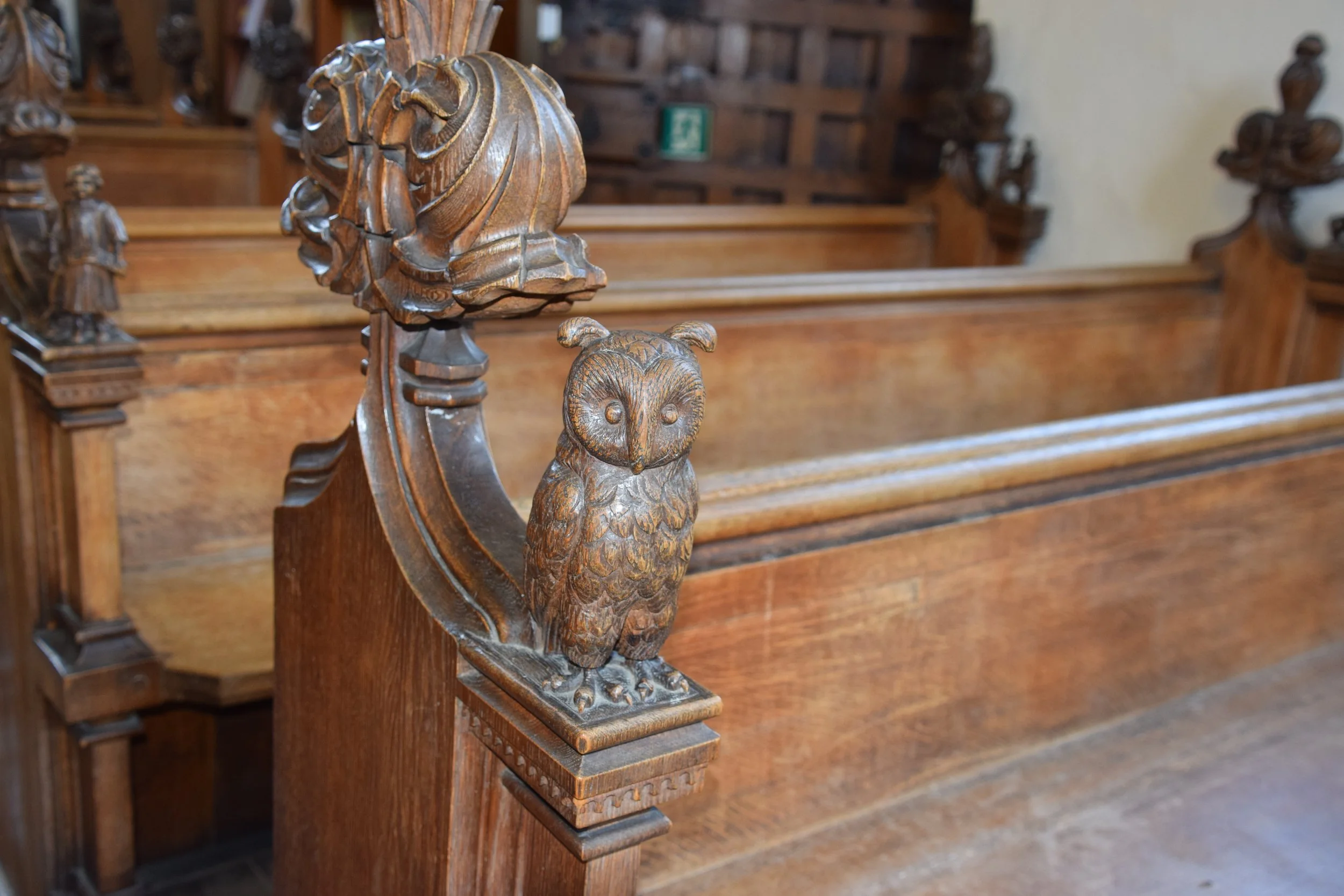 Carved wooden owl ornament on a church pew with lion carvings in the background