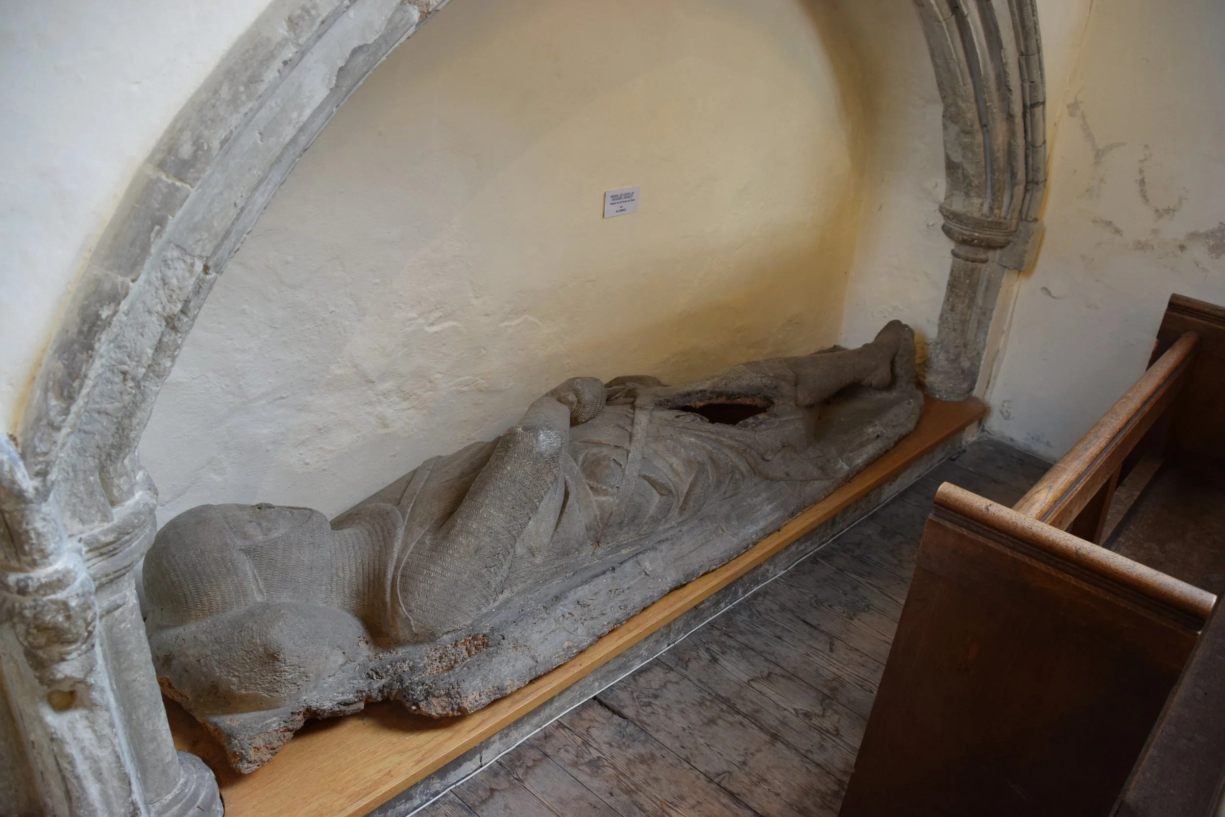 Medieval stone effigy of a reclining armored knight displayed in a church alcove.