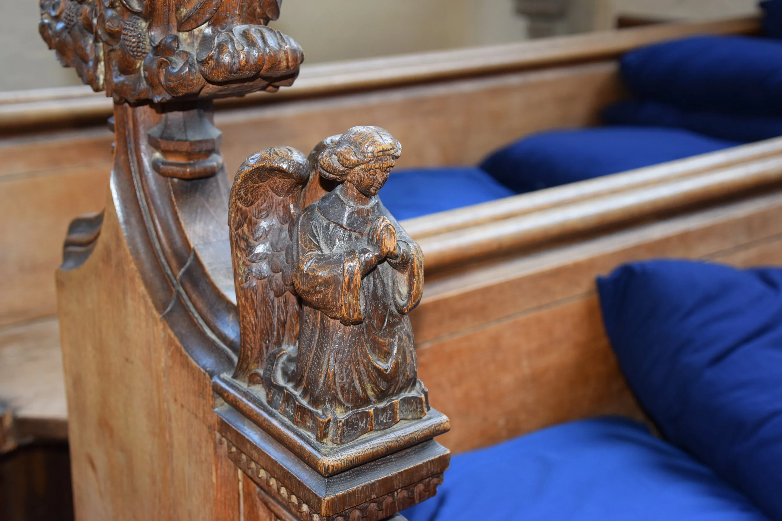 Close-up of ornate carved wooden church pew ends with religious figures and blue upholstered seats